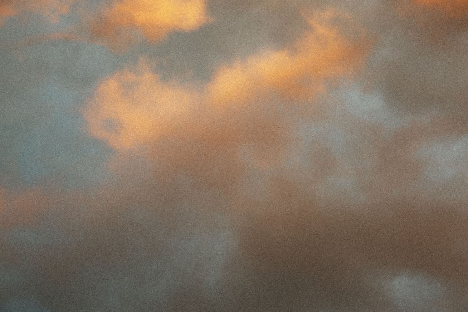 Dramatic sunset sky with warm orange and golden clouds against a soft grey background.