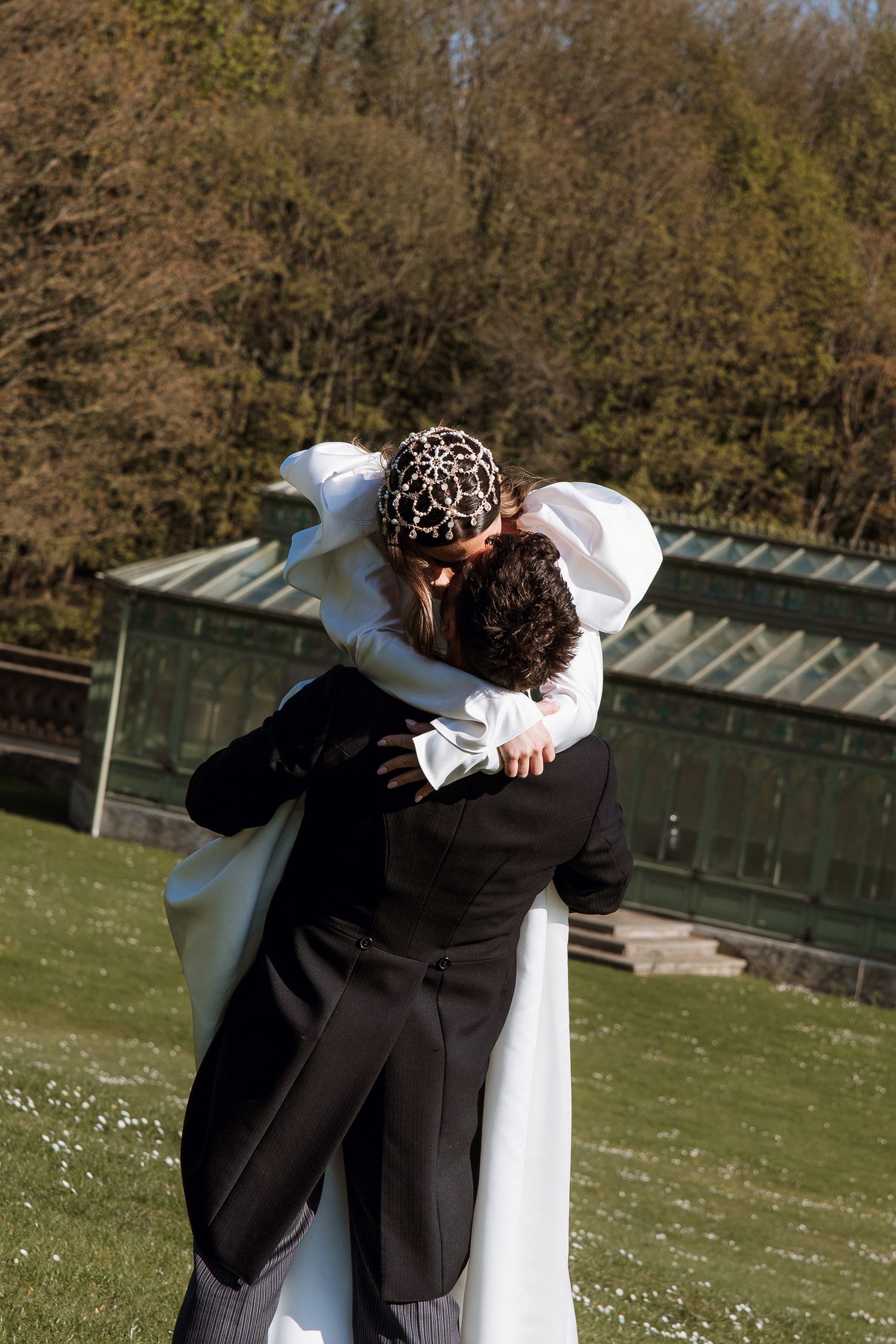 Bride and groom sharing a romantic kiss outdoors on their wedding day, surrounded by lush green trees.