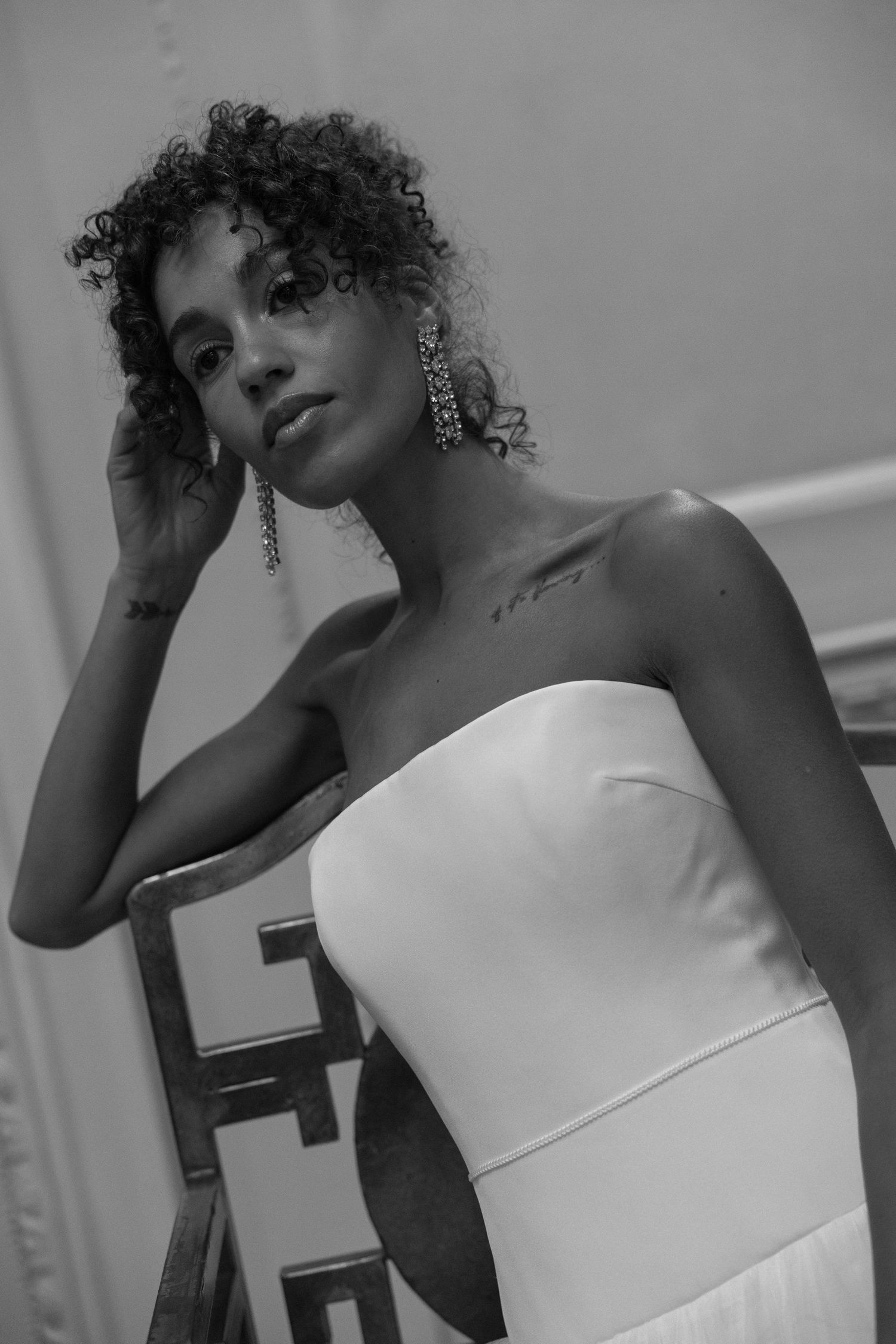 Black and white portrait of a bride in strapless white gown with curly hair and chandelier earrings.