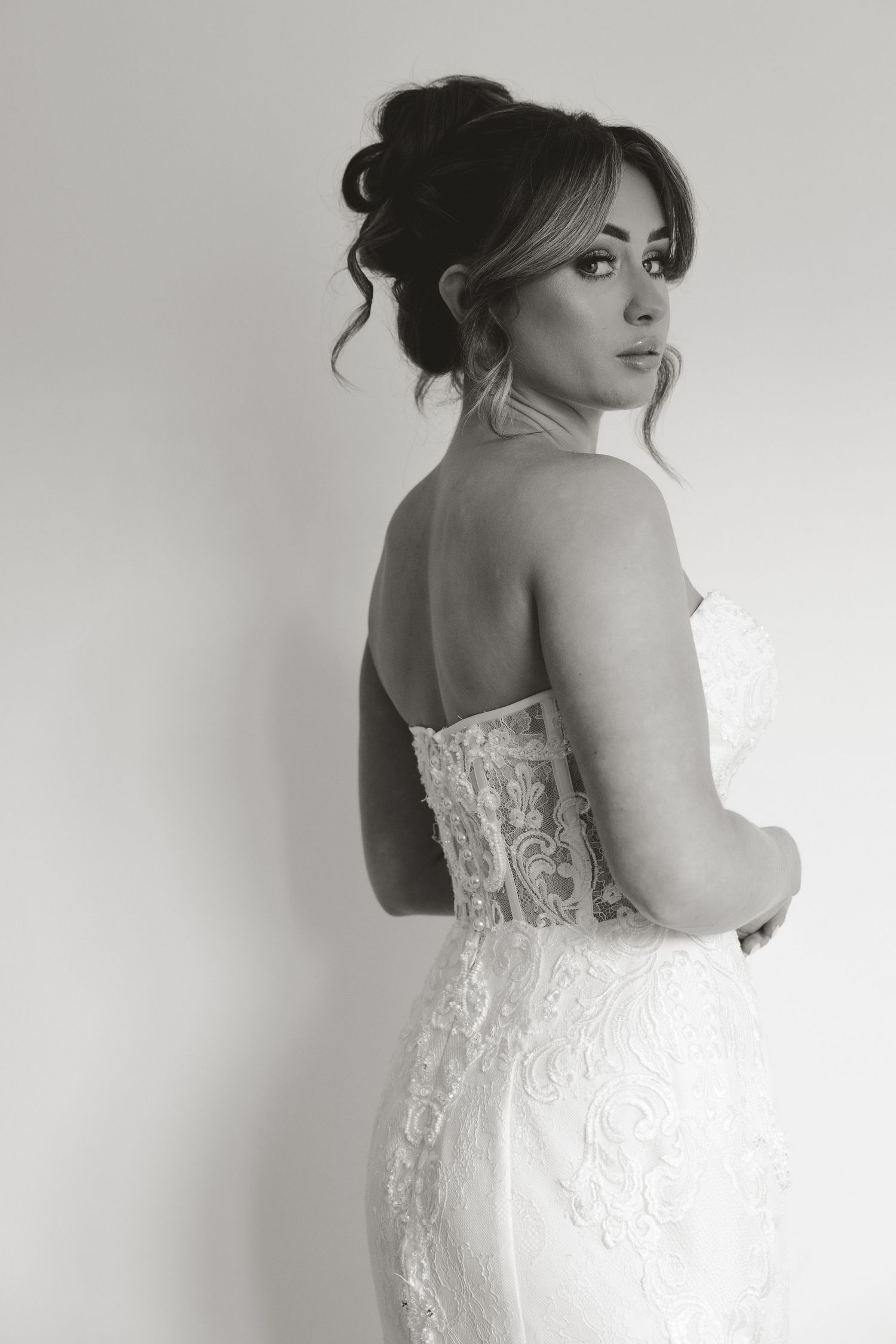 Black and white photo of a bride in a strapless lace wedding gown, looking over her shoulder with an elegant updo.