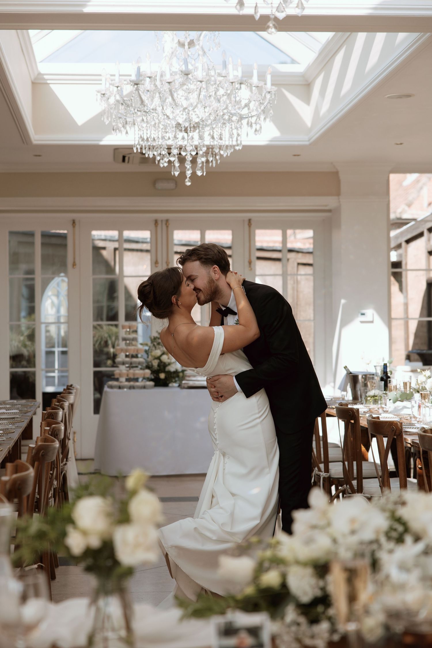 Bride and groom sharing a romantic dip kiss under a crystal chandelier in a beautifully decorated reception.