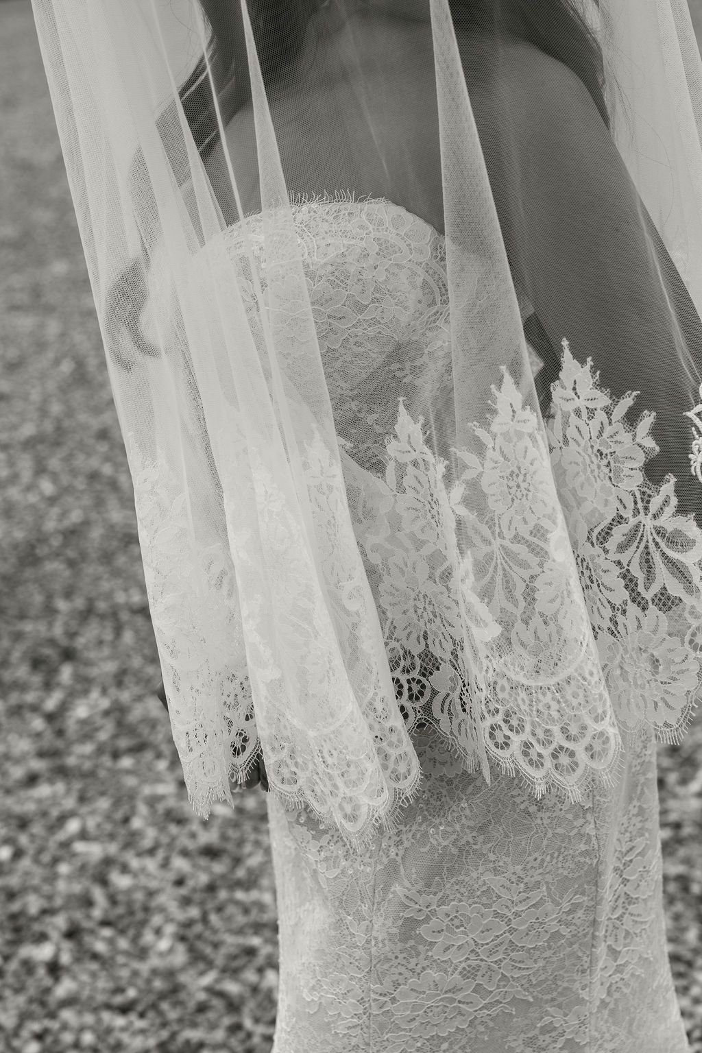 Black and white close-up of a bride in a lace wedding dress with an intricate lace-trimmed veil.