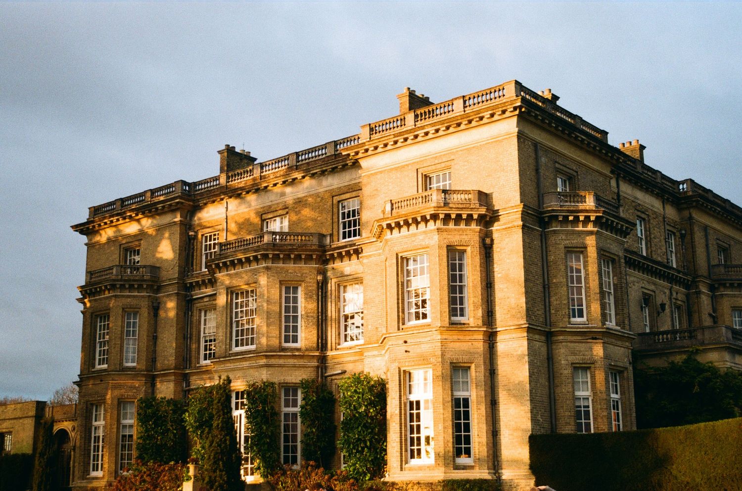 Grand historic stone manor house bathed in warm golden sunset light, elegant wedding venue exterior.