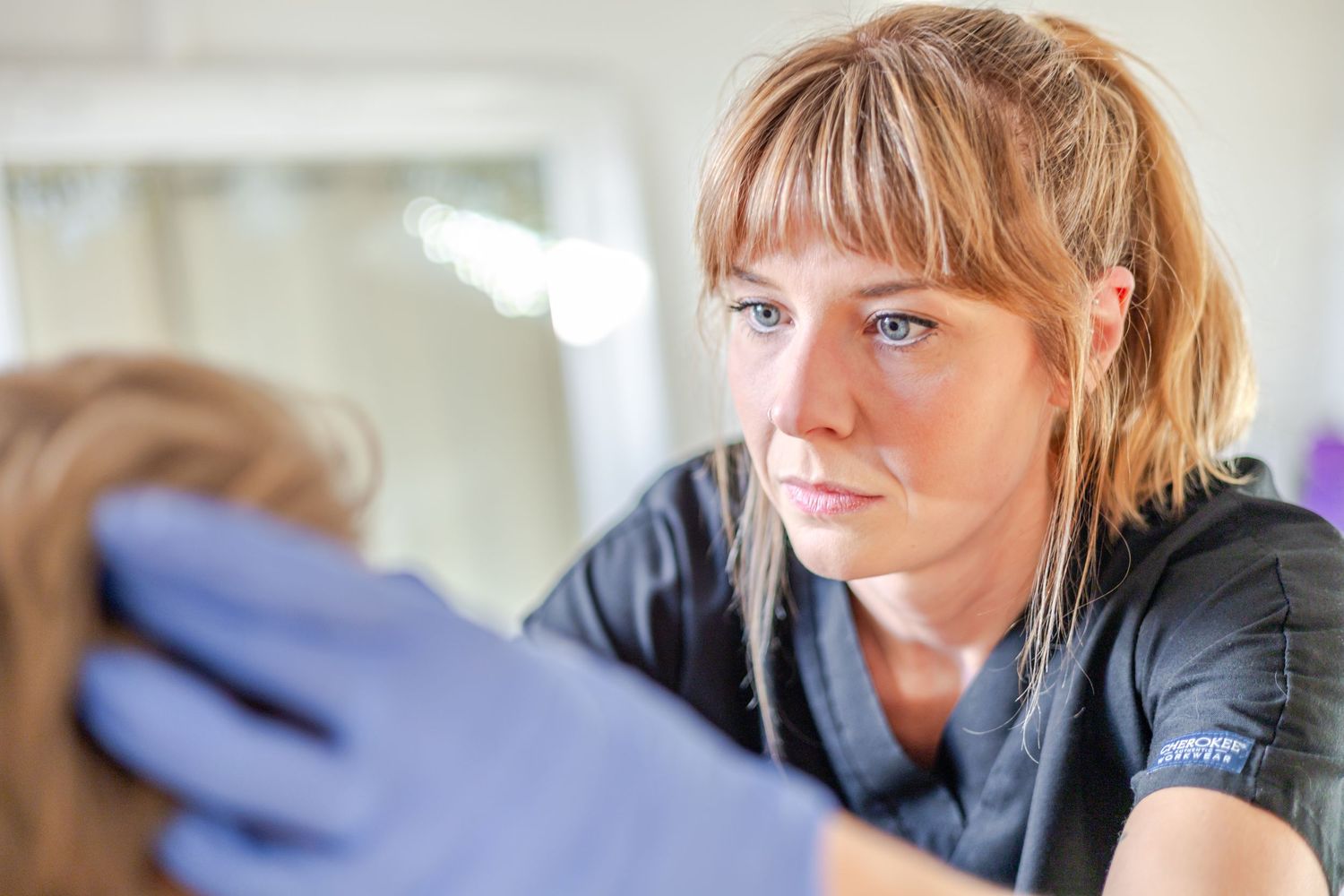 Female healthcare professional wearing blue gloves closely examining a patients hair or scalp.