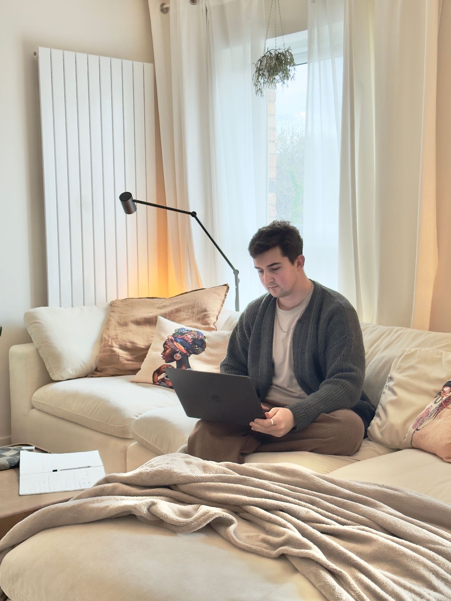 Young man sitting on a cream sofa using a laptop in a cozy warmly lit modern living room.