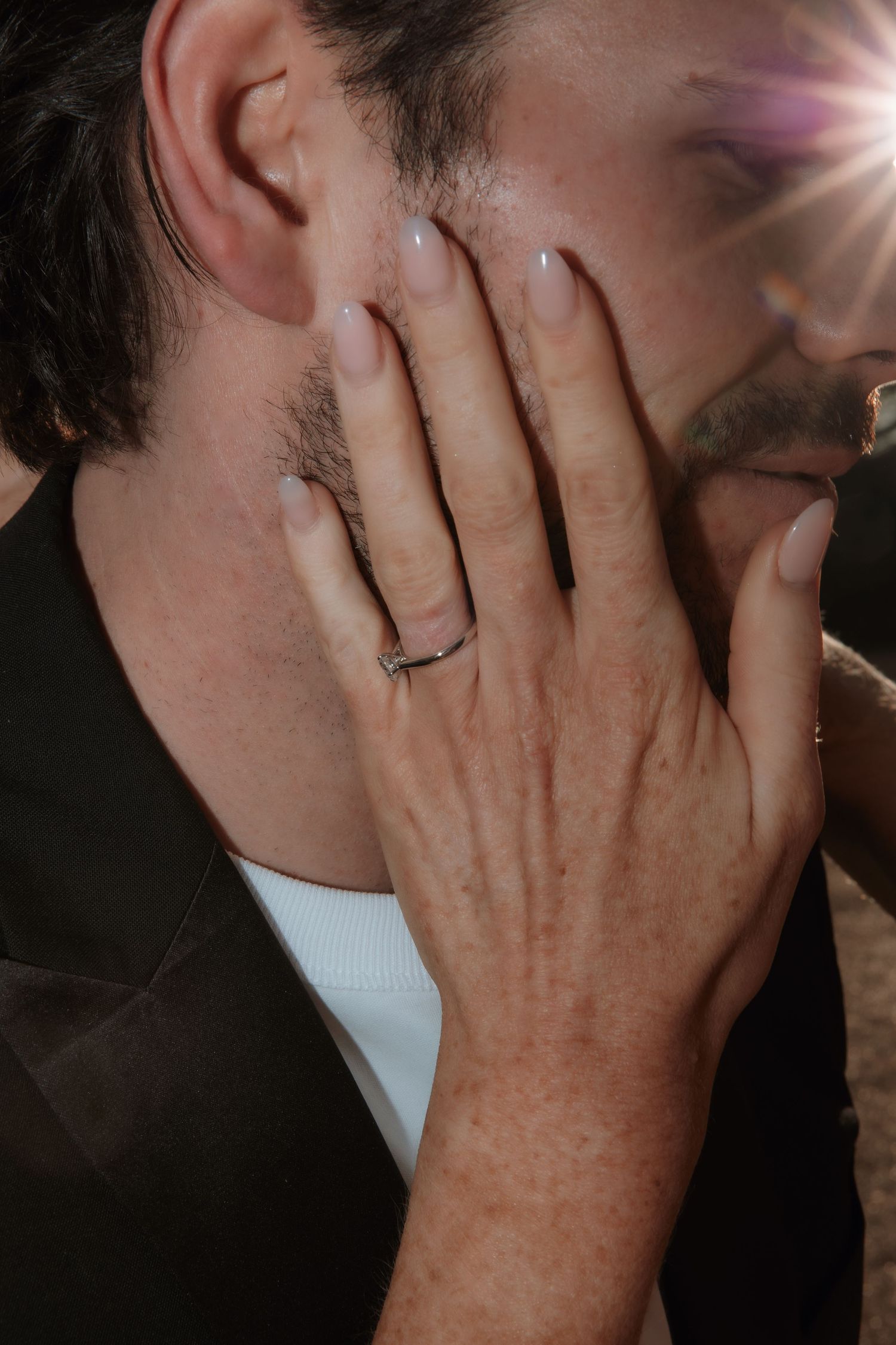 Close-up of a bride's hand with a diamond wedding ring gently touching the groom's face.