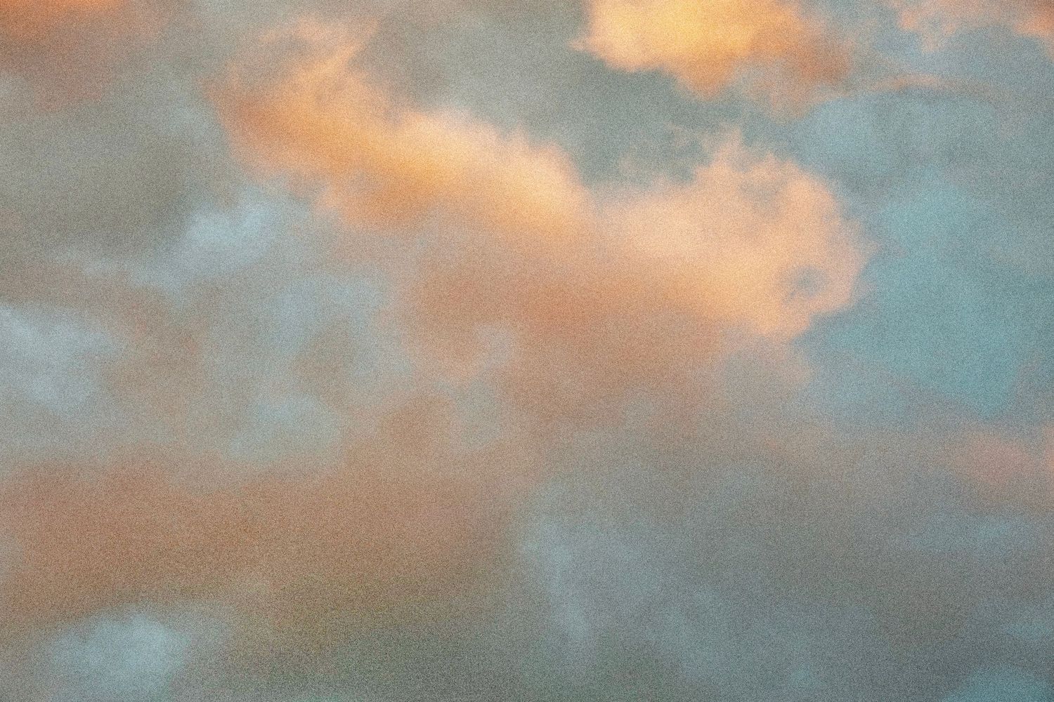 Soft pastel sunset sky with fluffy clouds illuminated in warm orange and pink hues against a blue-gray background.