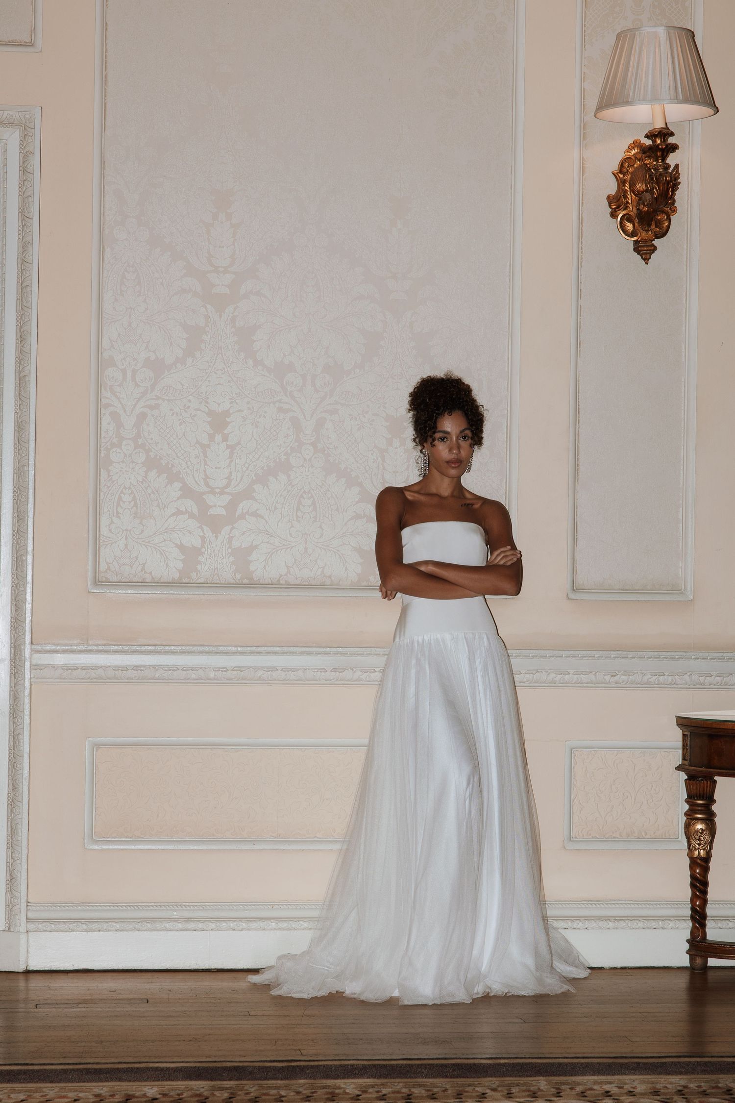Elegant bride in a white strapless tulle ballgown standing in a grand ornate ballroom.