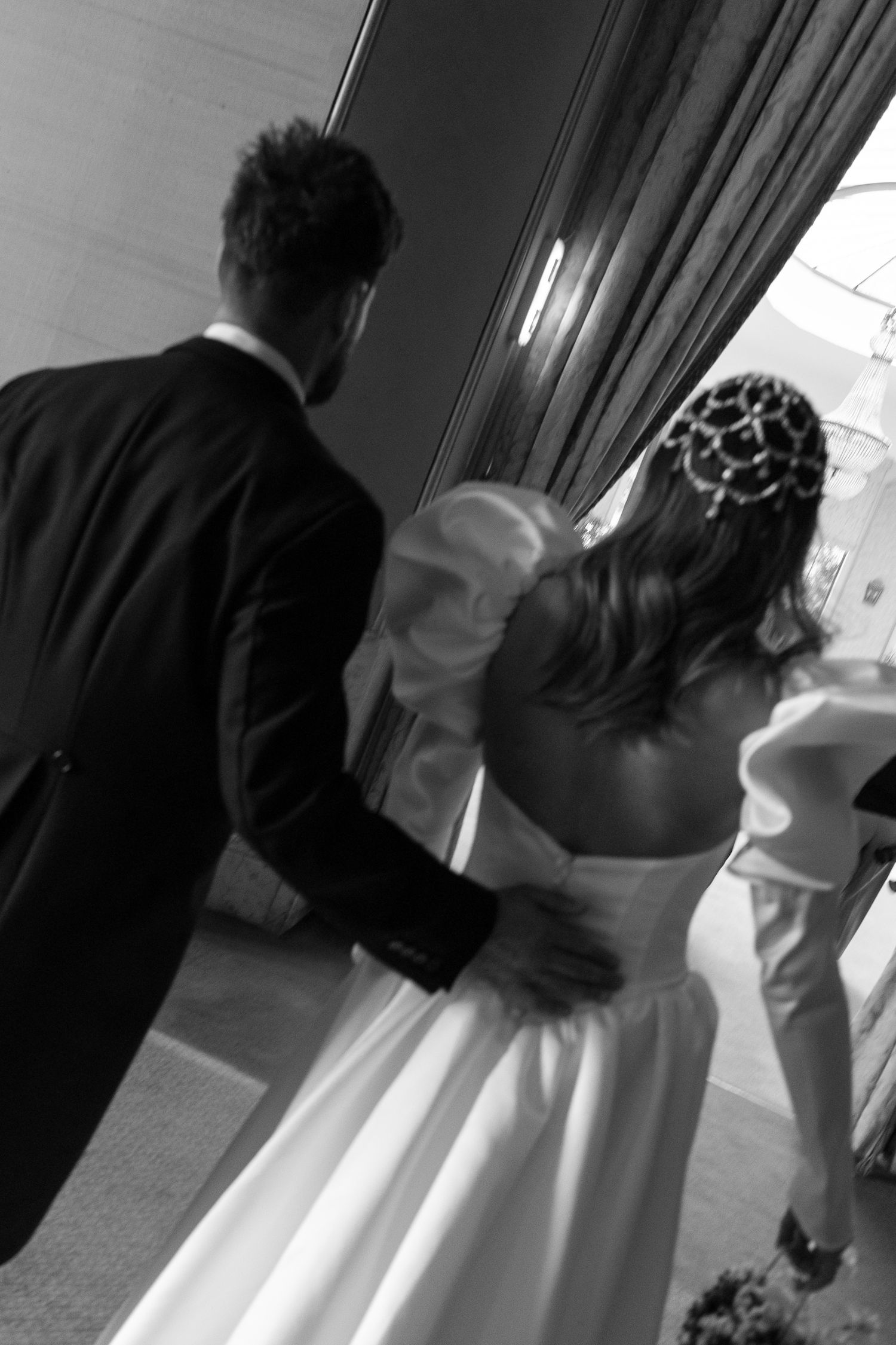 Black and white photo of bride and groom walking together, bride wearing elegant white gown and pearl headpiece.