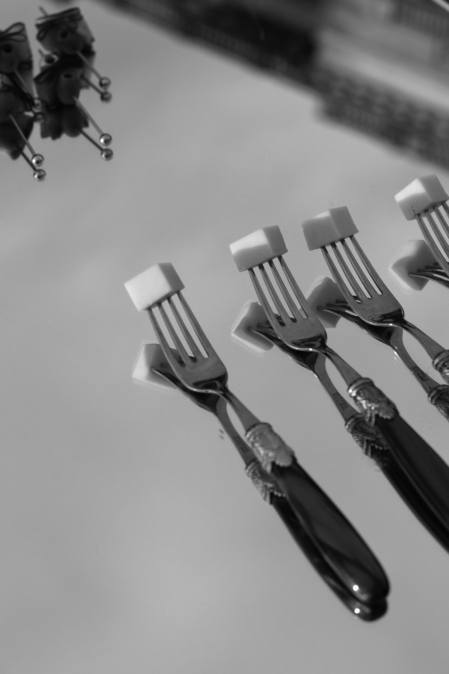 Black and white photo of elegant forks with sugar cubes arranged on a white table.