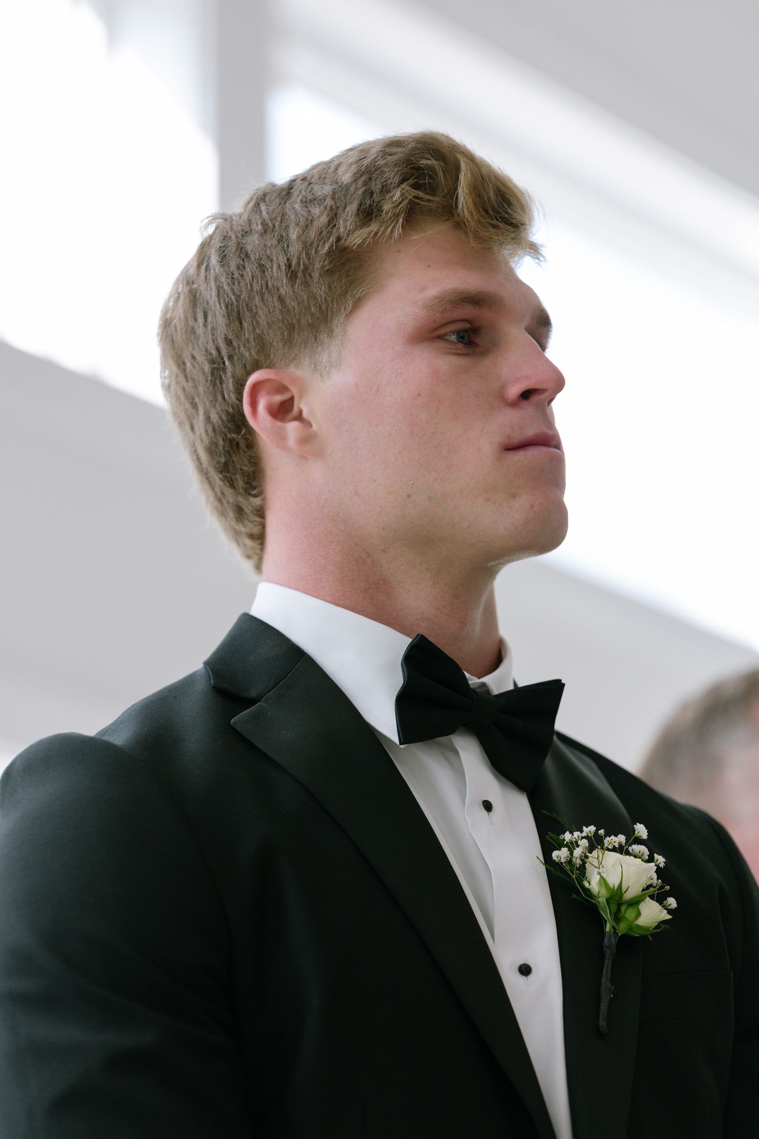 Emotional groom in black tuxedo with white boutonniere watching his bride walk down the aisle.