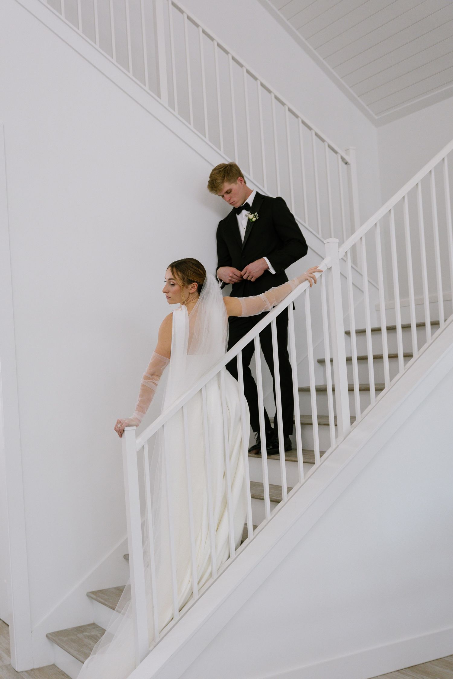 Bride and groom descend a white staircase together in a bright, elegant wedding venue.
