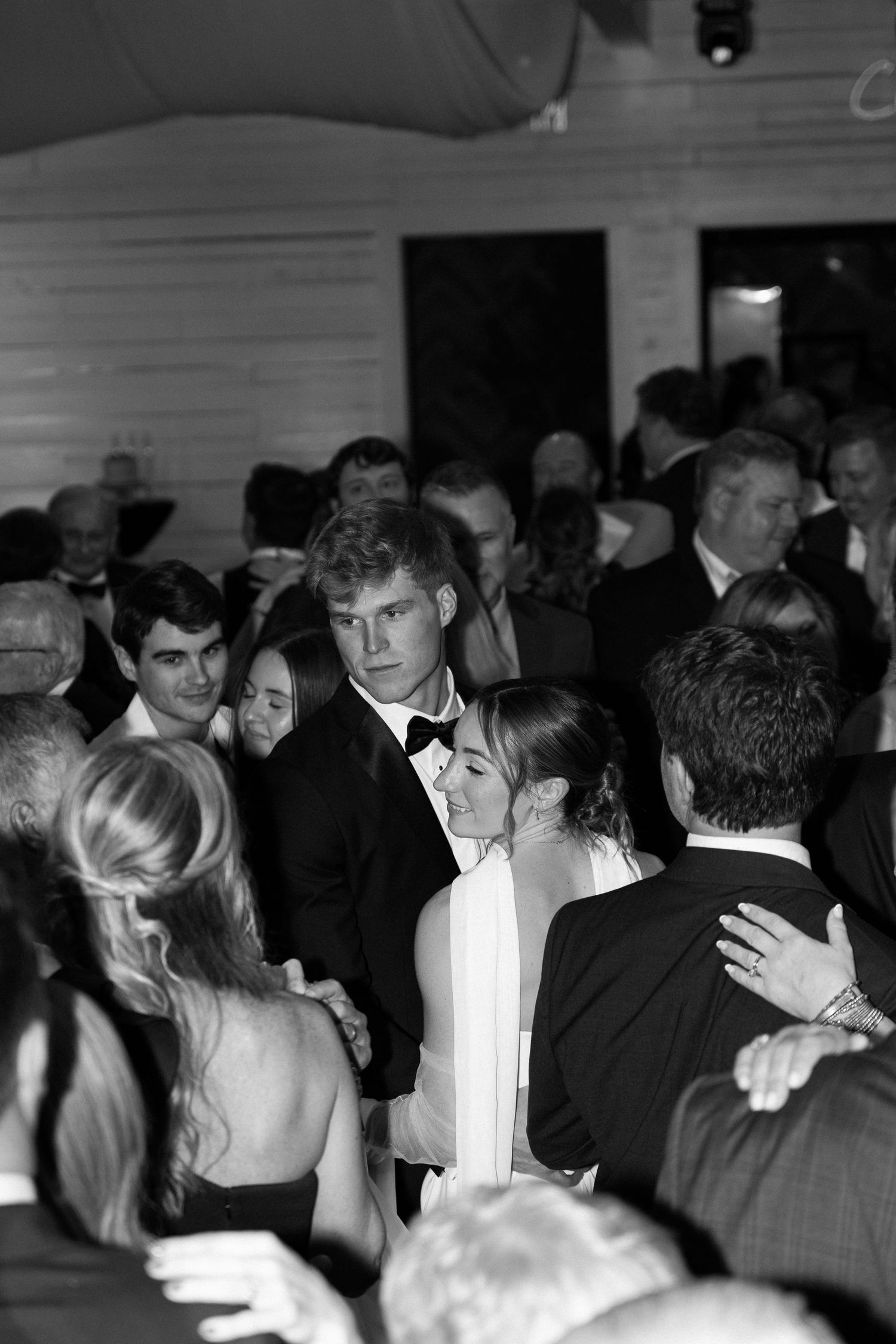 Bride and groom dancing together surrounded by wedding guests on crowded reception dance floor.
