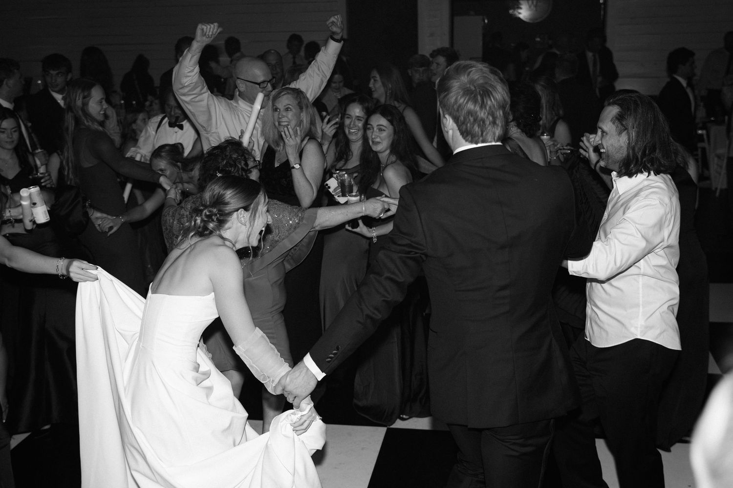Bride and groom celebrate with guests on the dance floor during a lively black and white wedding reception.
