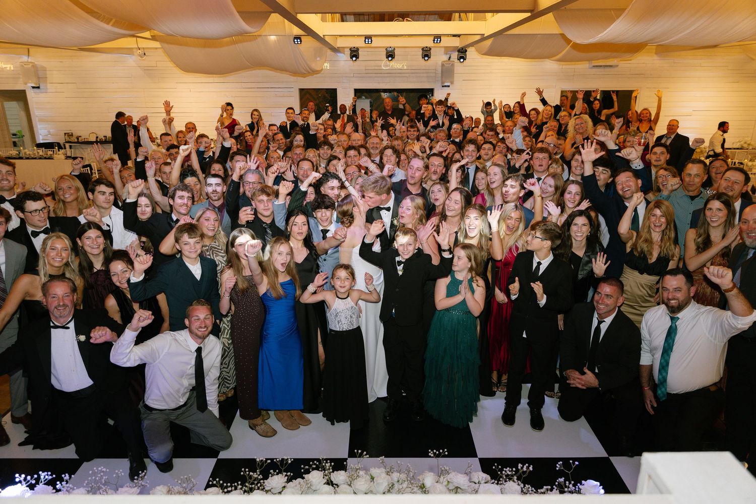 Large wedding reception group photo with hundreds of guests celebrating on white dance floor.