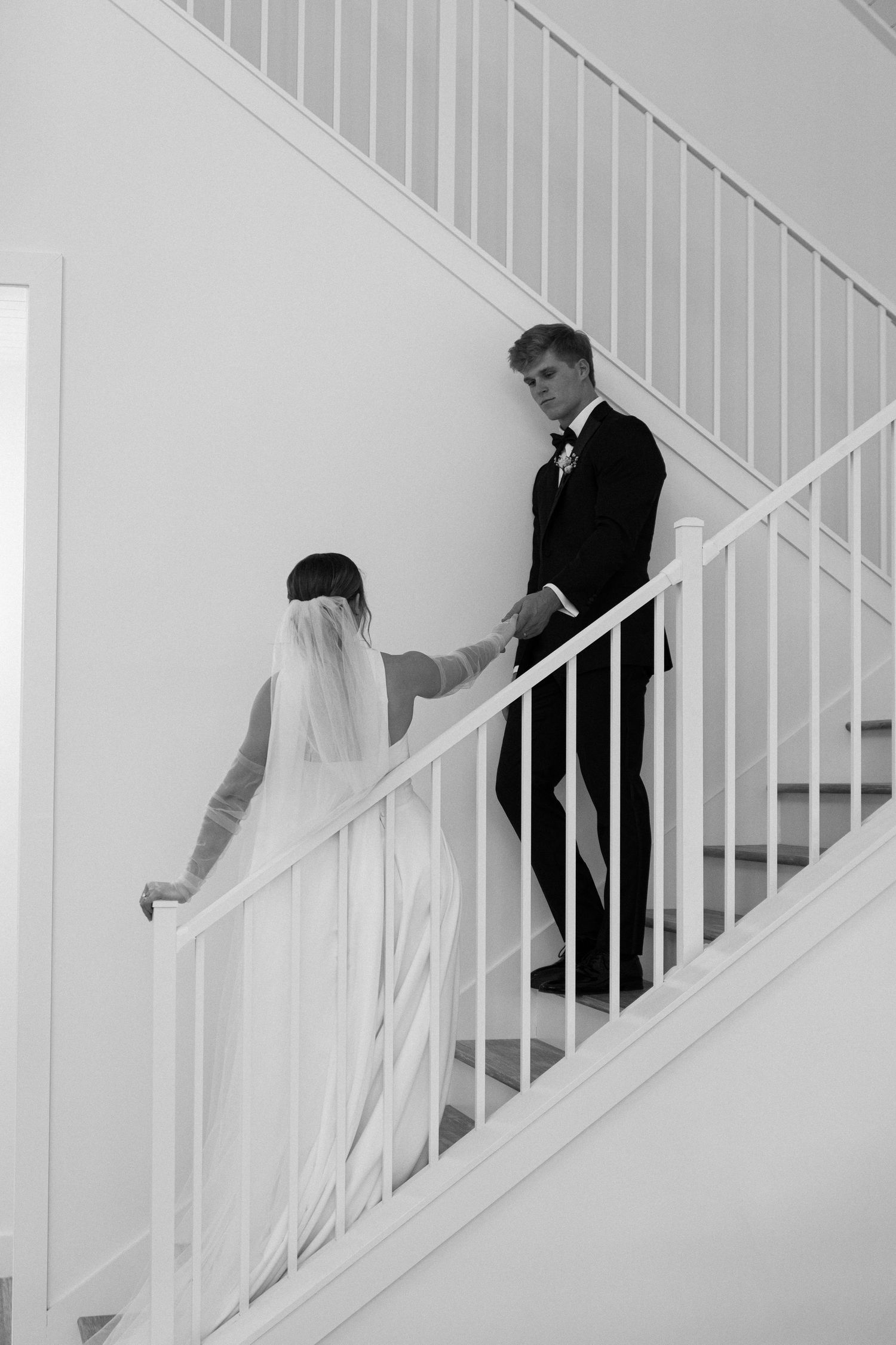 Bride and groom holding hands while ascending a white staircase in black and white wedding photo.