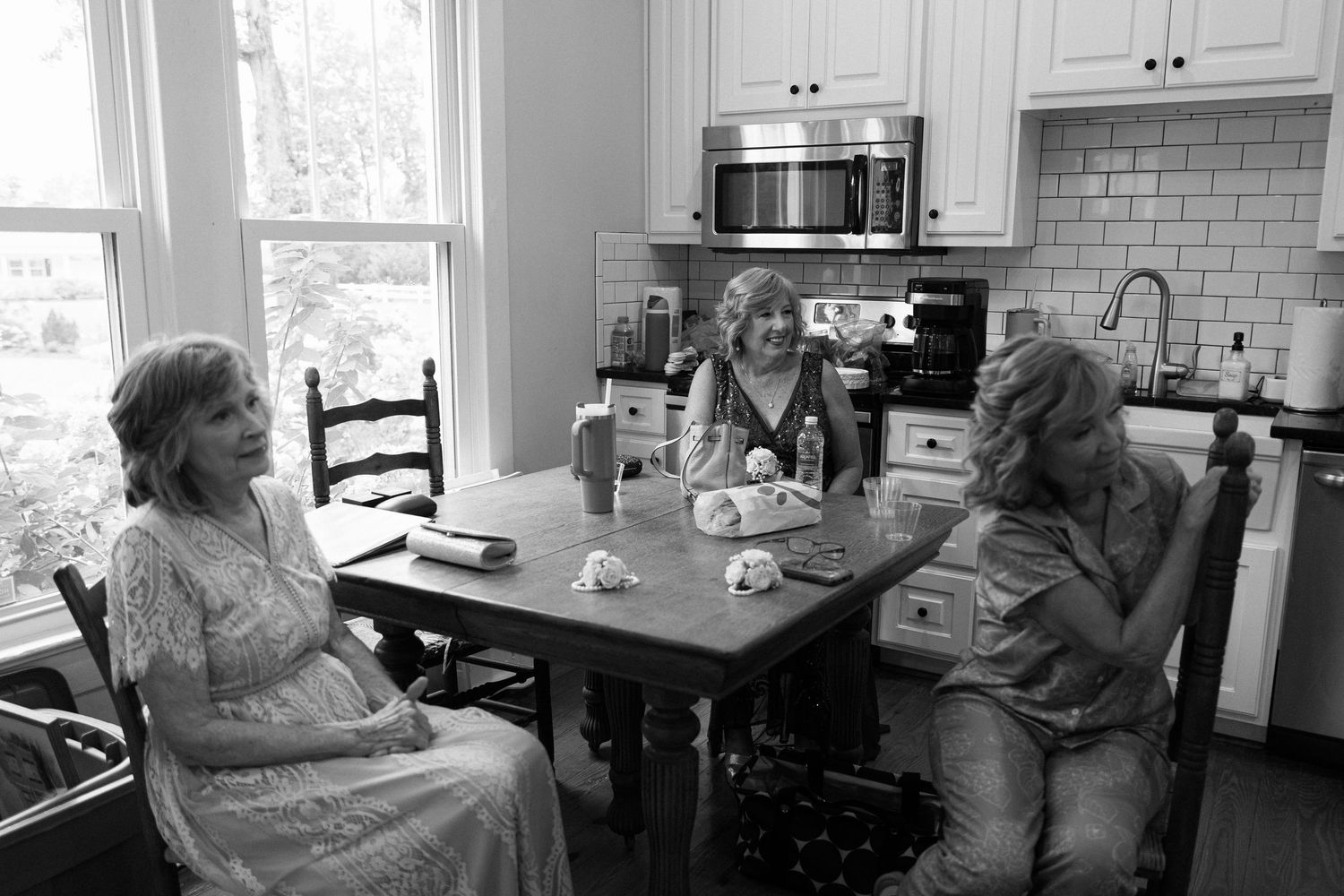 Three women sharing a joyful conversation at a kitchen table in a bright, modern home.
