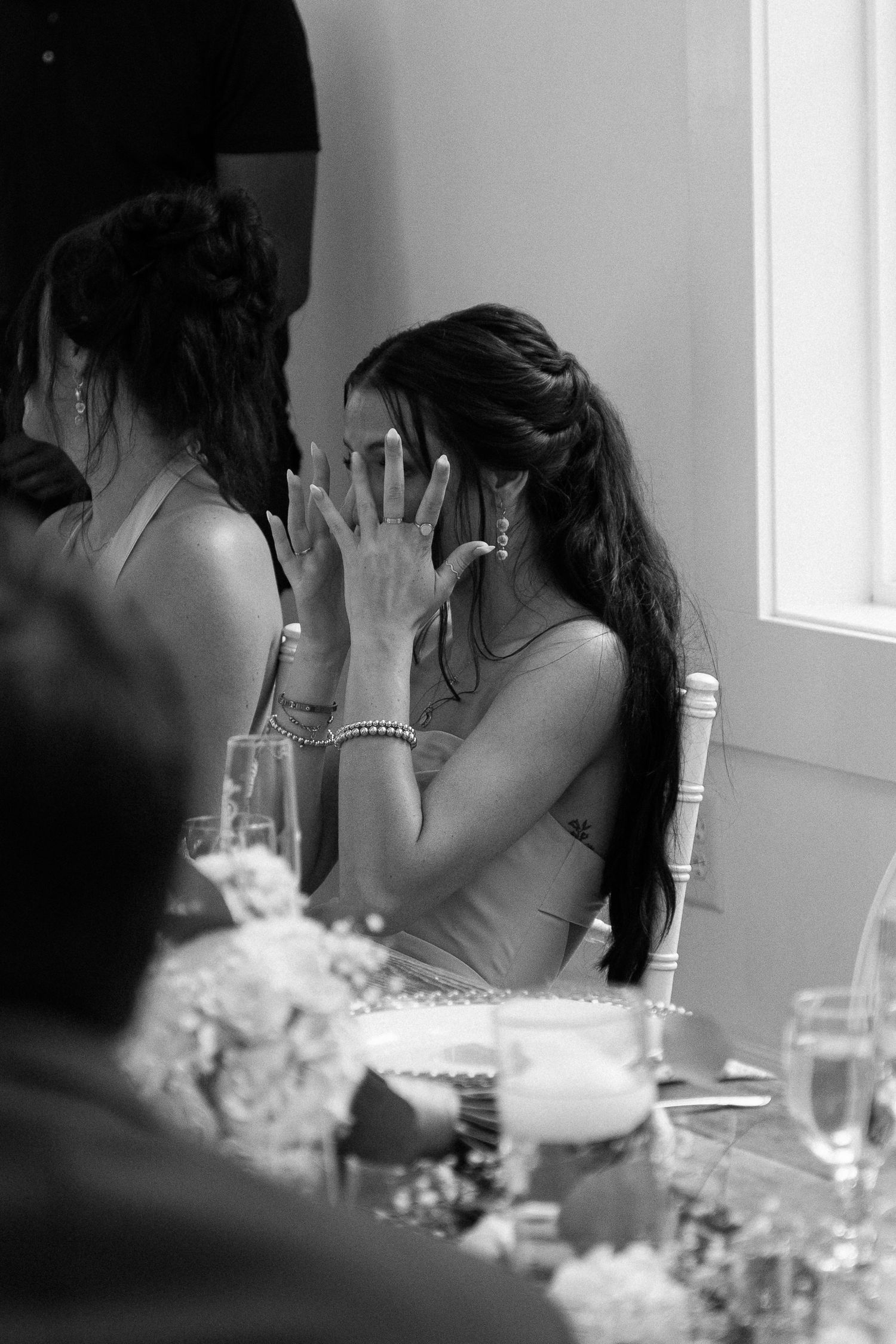 Black and white photo of a woman covering her face with her hands at a wedding reception table.