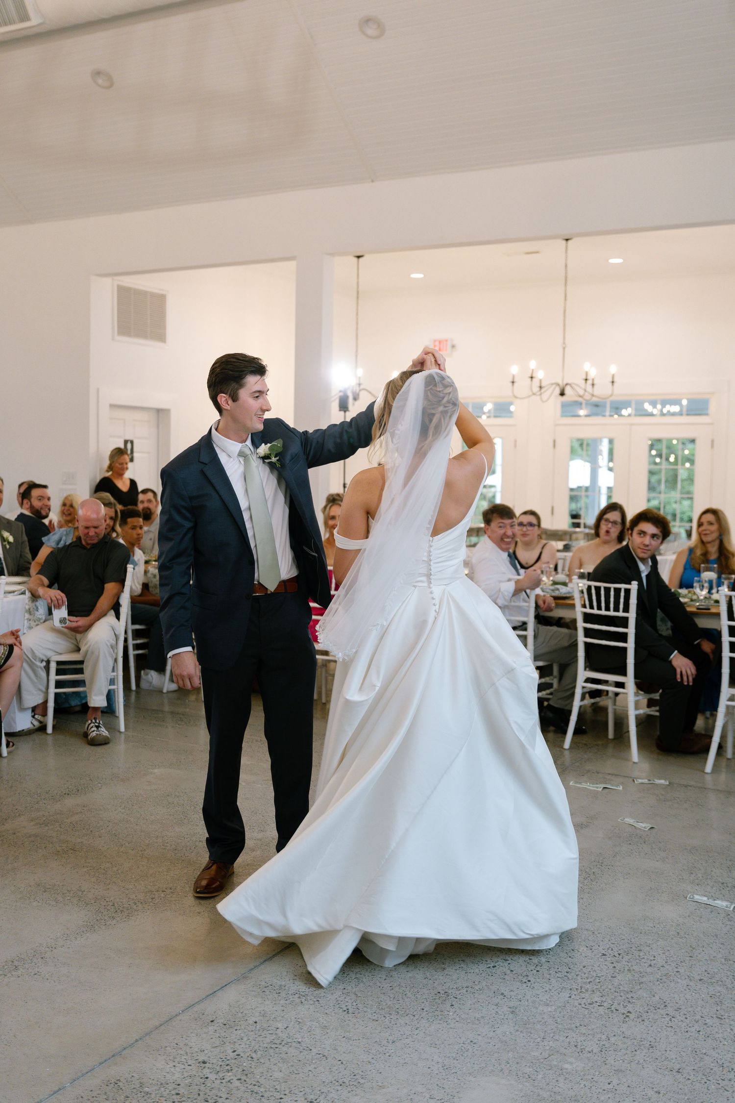 Groom twirling bride in a flowing white gown and veil during their first dance at wedding reception.