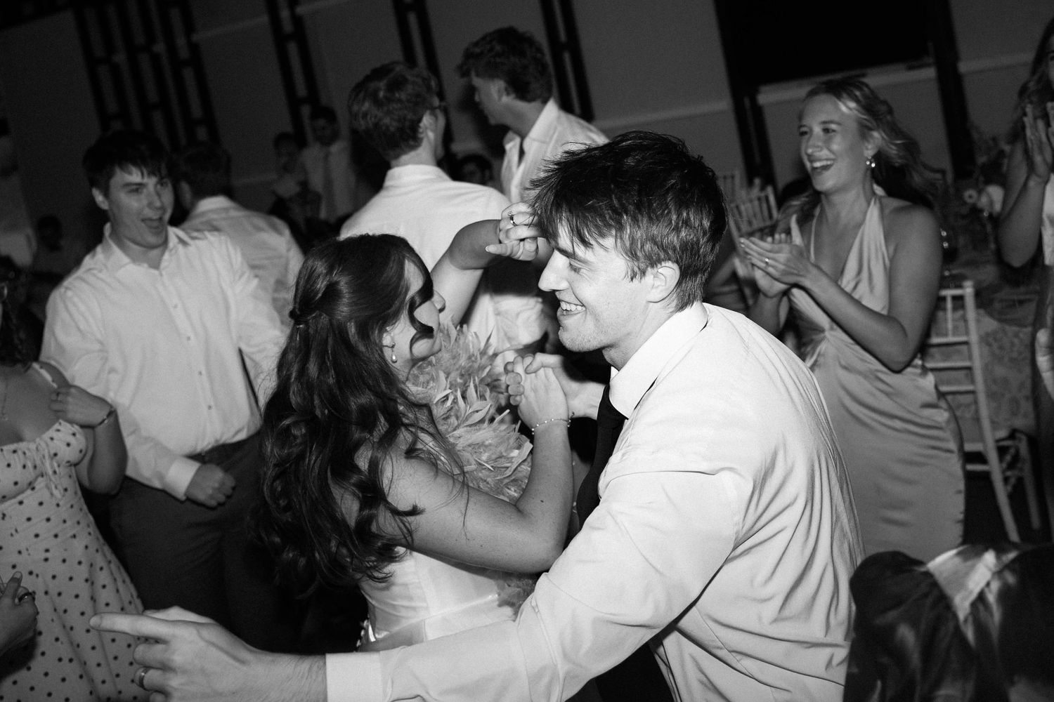 Black and white photo of a couple dancing closely at a wedding reception, surrounded by guests celebrating.