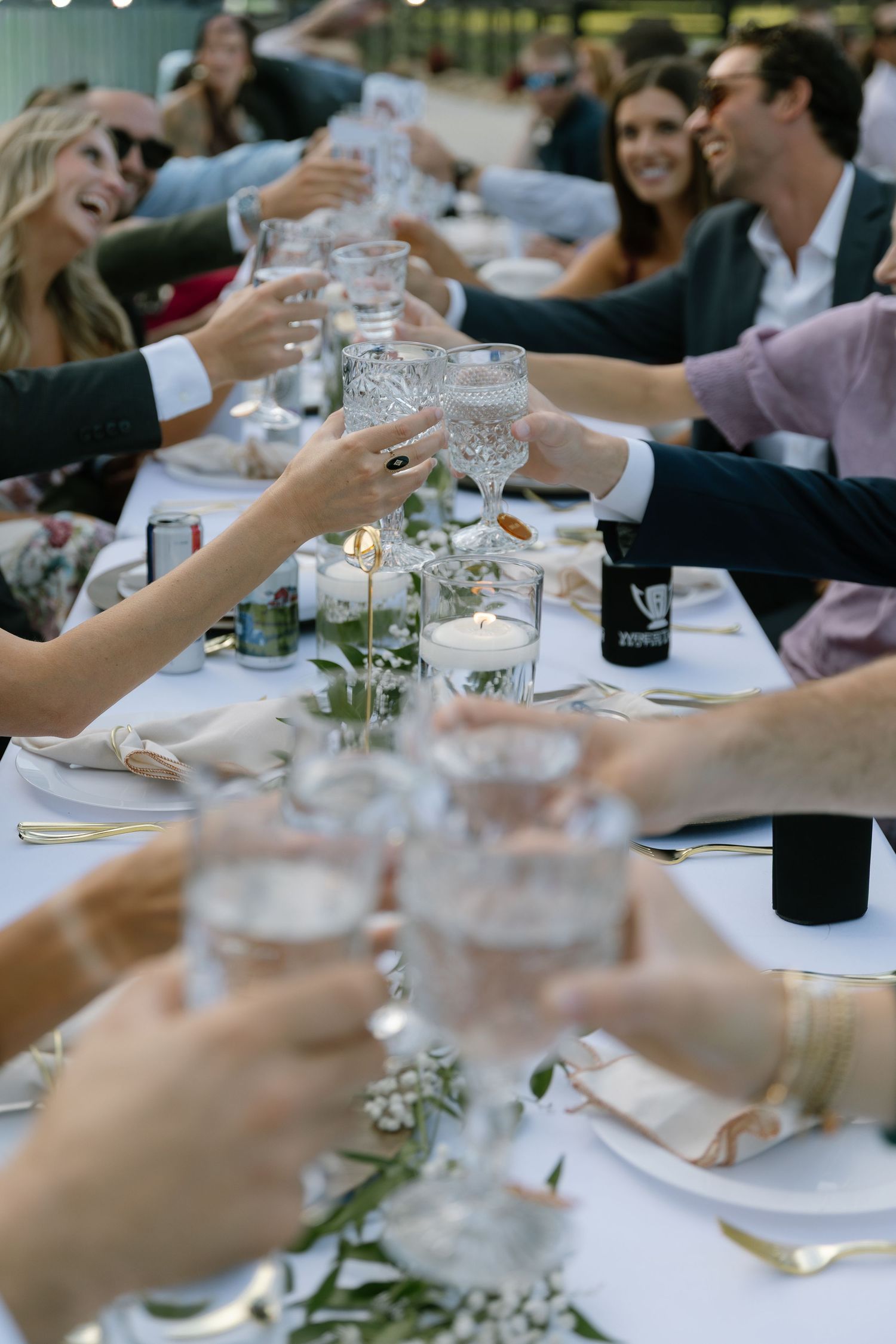 Guests raising crystal glasses in a celebratory toast at an elegant outdoor wedding reception dinner table.
