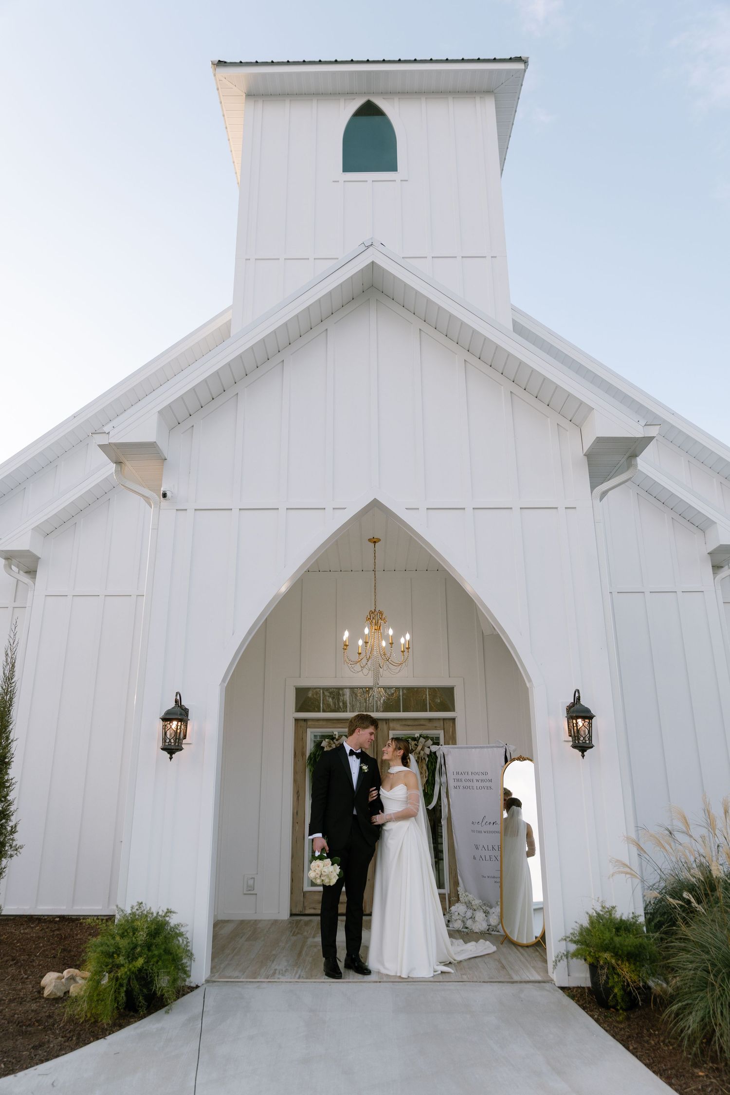 Bride and groom share a romantic moment in the arched entrance of a white chapel wedding venue.