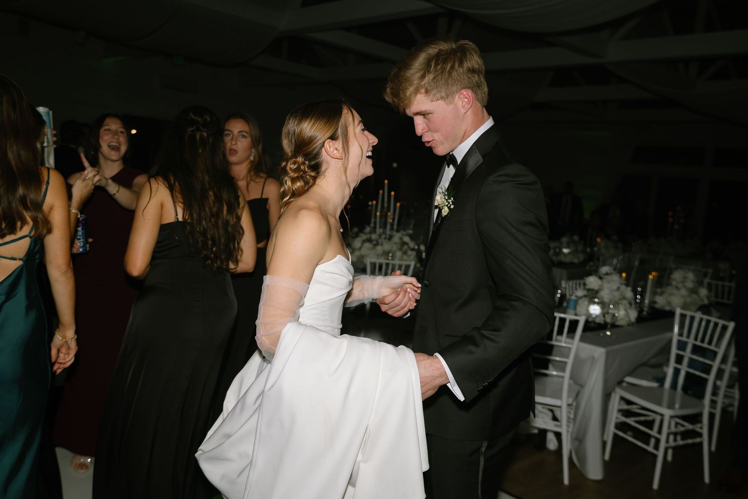 Bride and groom share a dance surrounded by guests at their lively wedding reception.