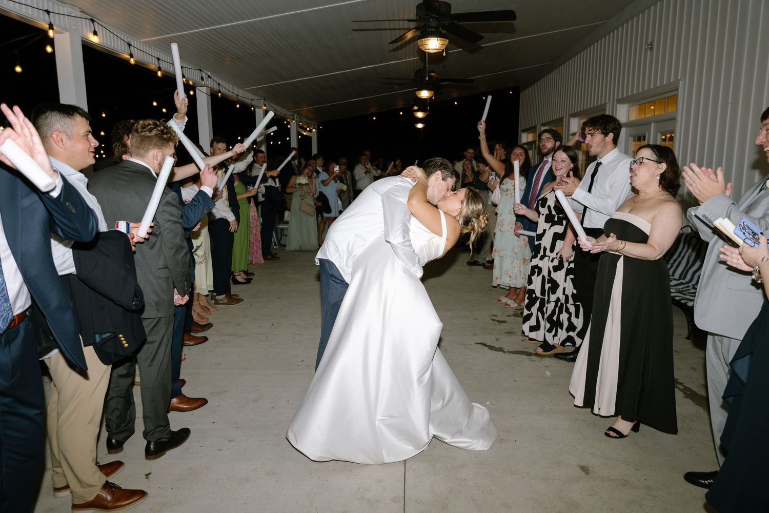 Bride and groom share romantic dip kiss during grand exit with cheering guests lining the aisle.