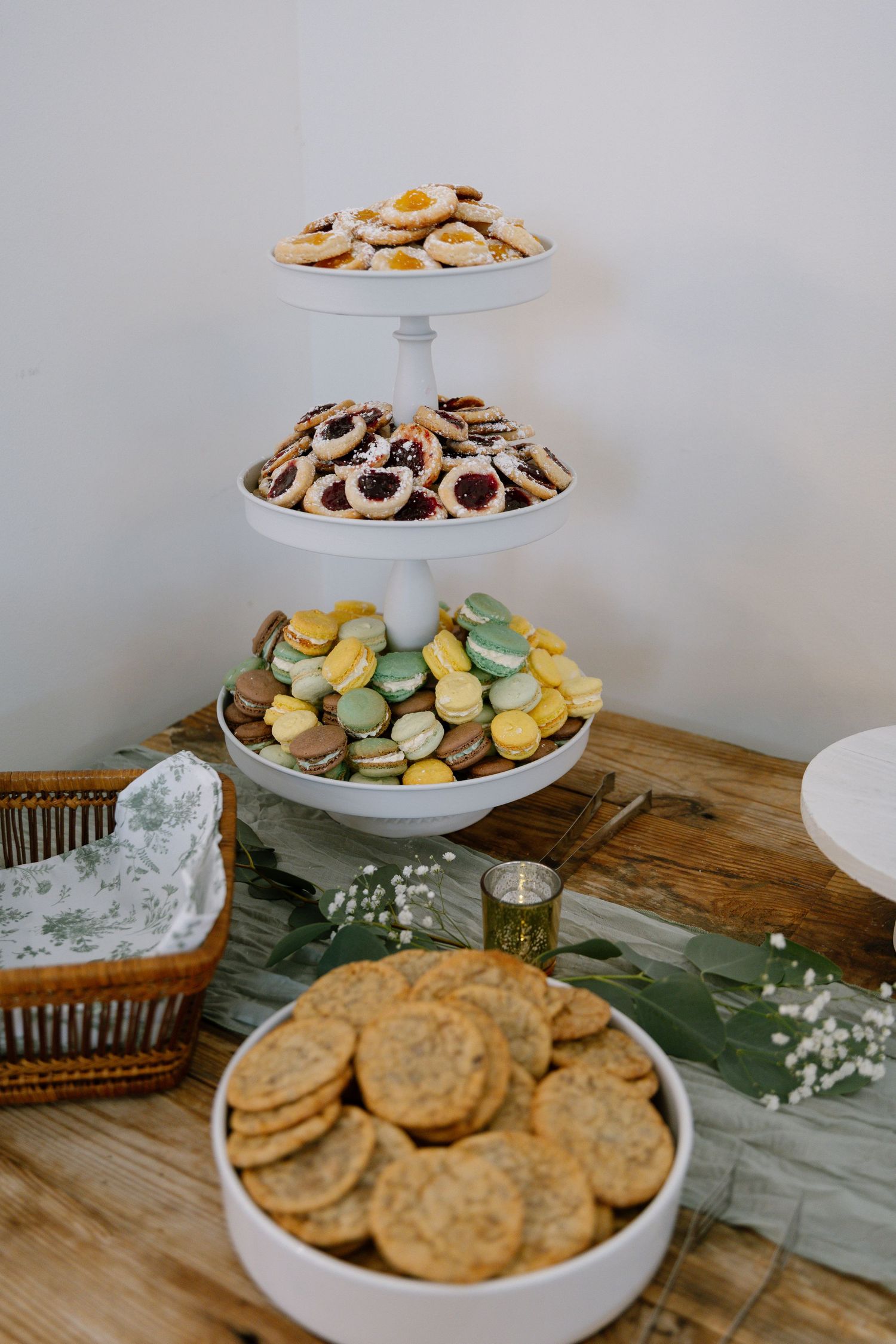 Three-tier white stand displays colorful macarons, linzer cookies, and shortbread at an elegant wedding dessert table.