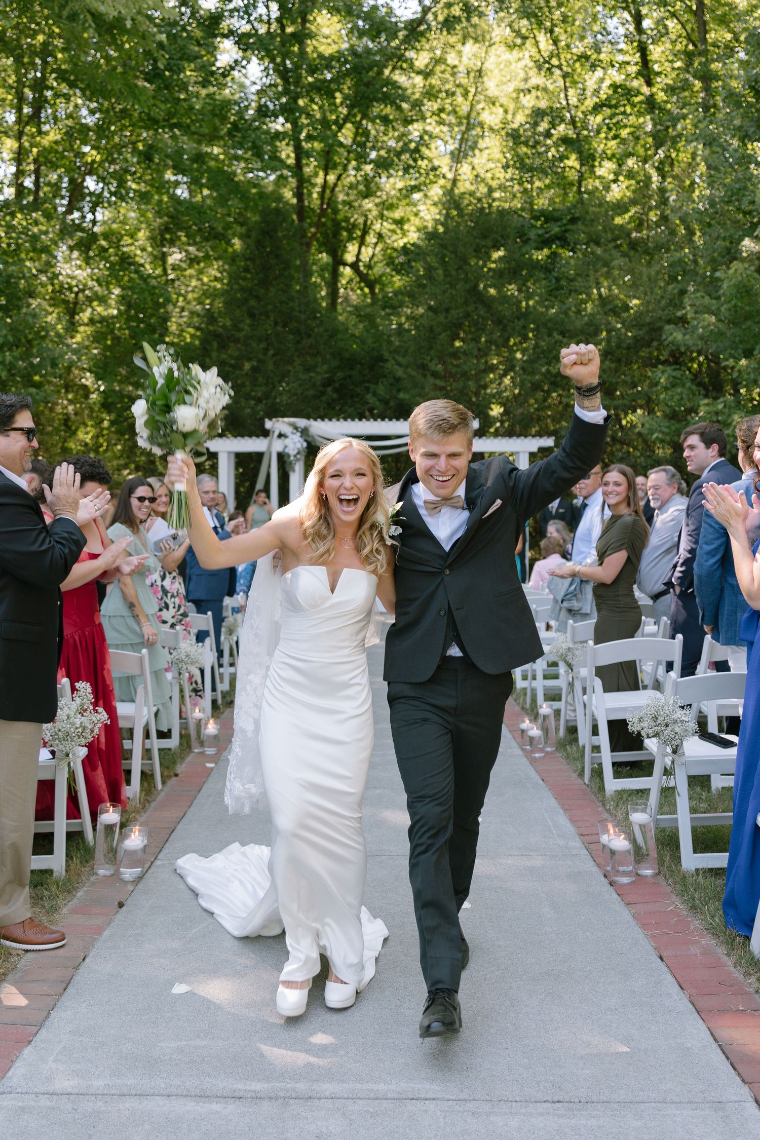 Joyful newlyweds celebrate their recessional walk down the aisle at an outdoor wedding ceremony surrounded by cheering guests.
