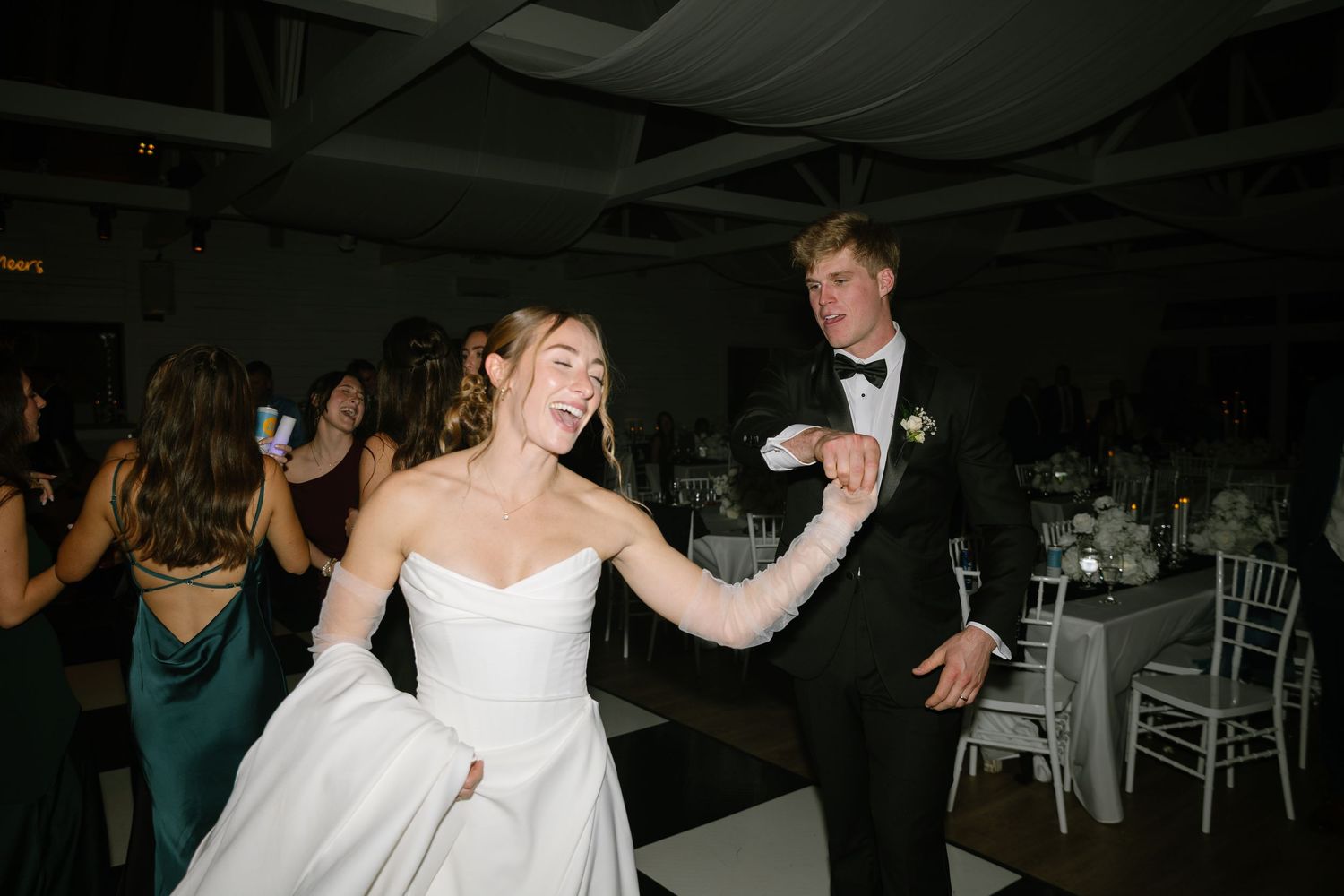 Joyful bride in white gown and gloves dancing with groom at lively wedding reception.