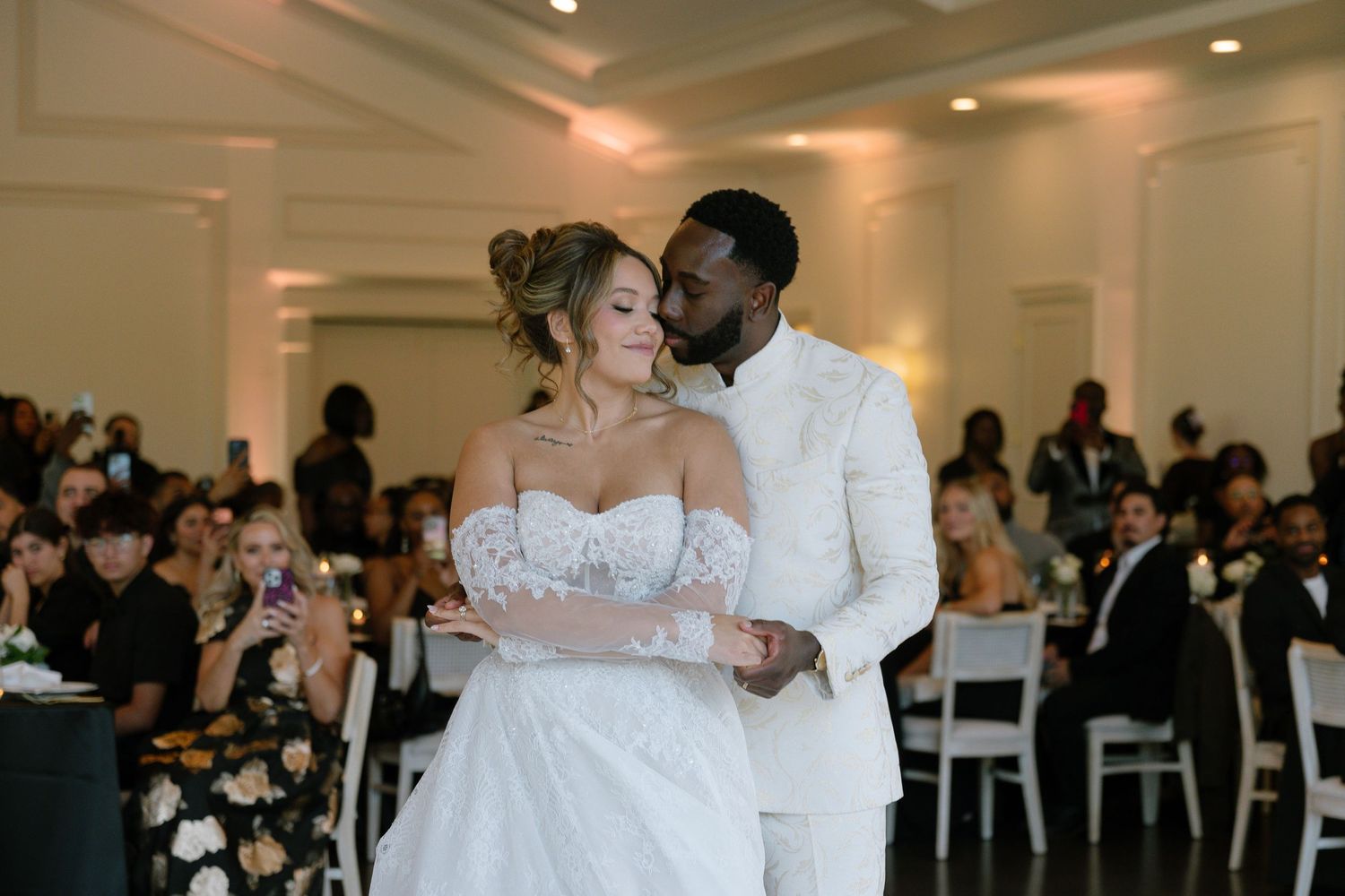 Bride and groom share a romantic first dance at elegant wedding reception in white ballroom.