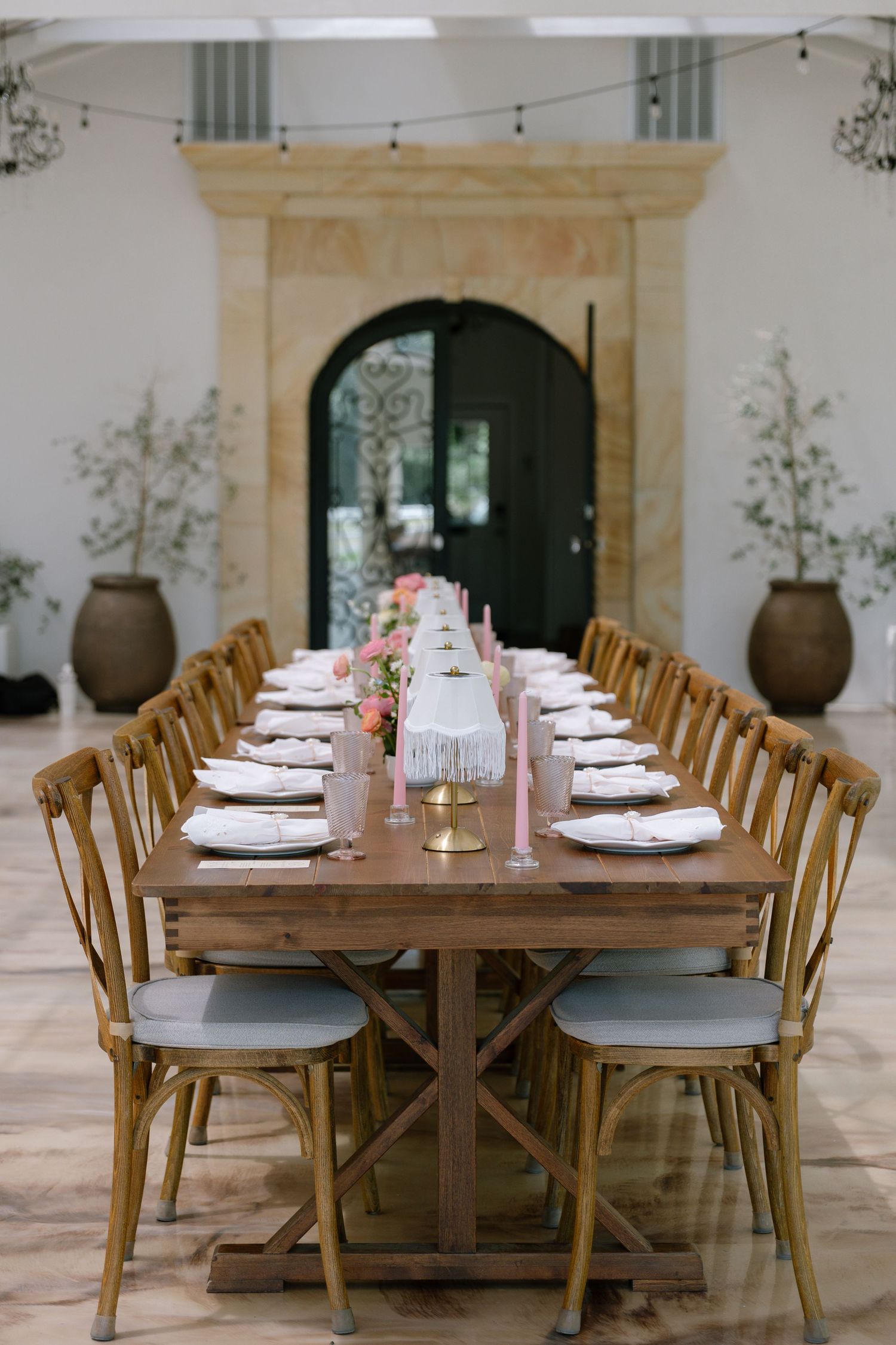 Elegant long wooden farmhouse table with pink candles, white plates, and floral centerpieces set for a wedding reception.