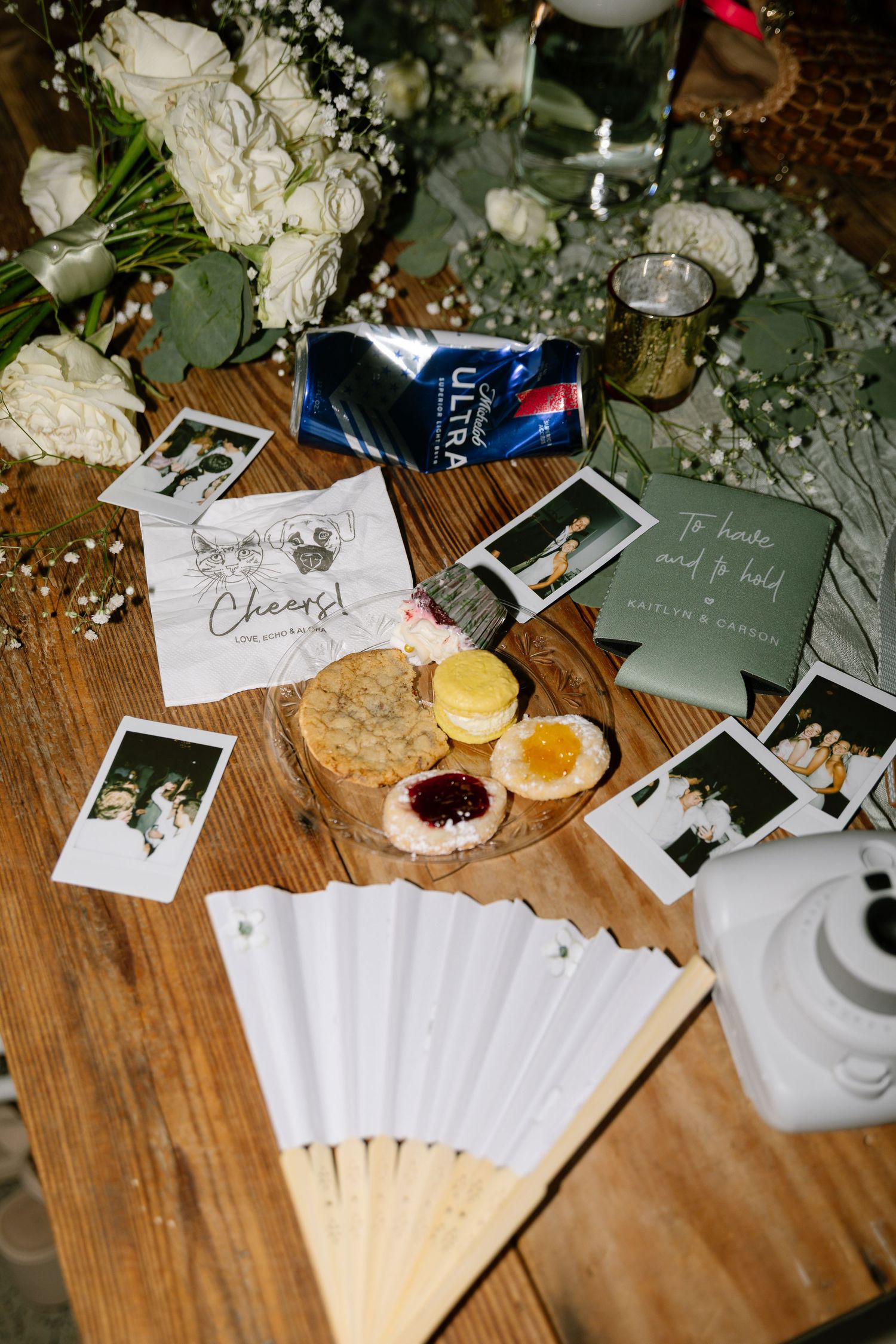 Wedding reception table with Polaroid photos, white fans, macarons, roses, and Michelob Ultra beer.