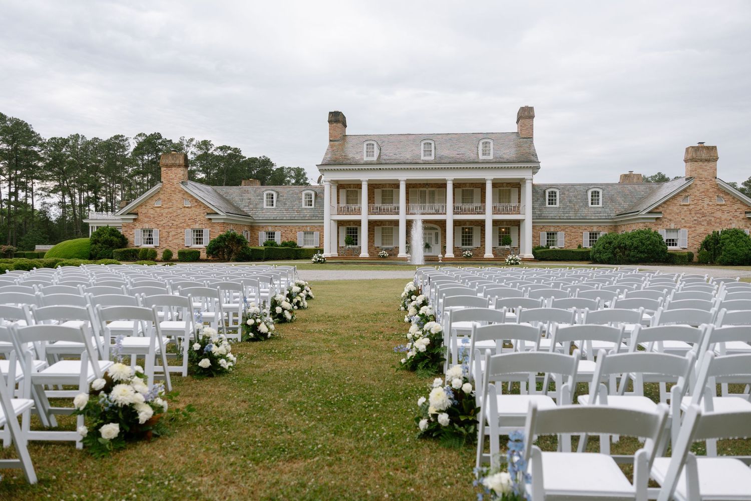 Elegant outdoor wedding ceremony setup with white chairs and floral aisle at a grand Southern plantation mansion.