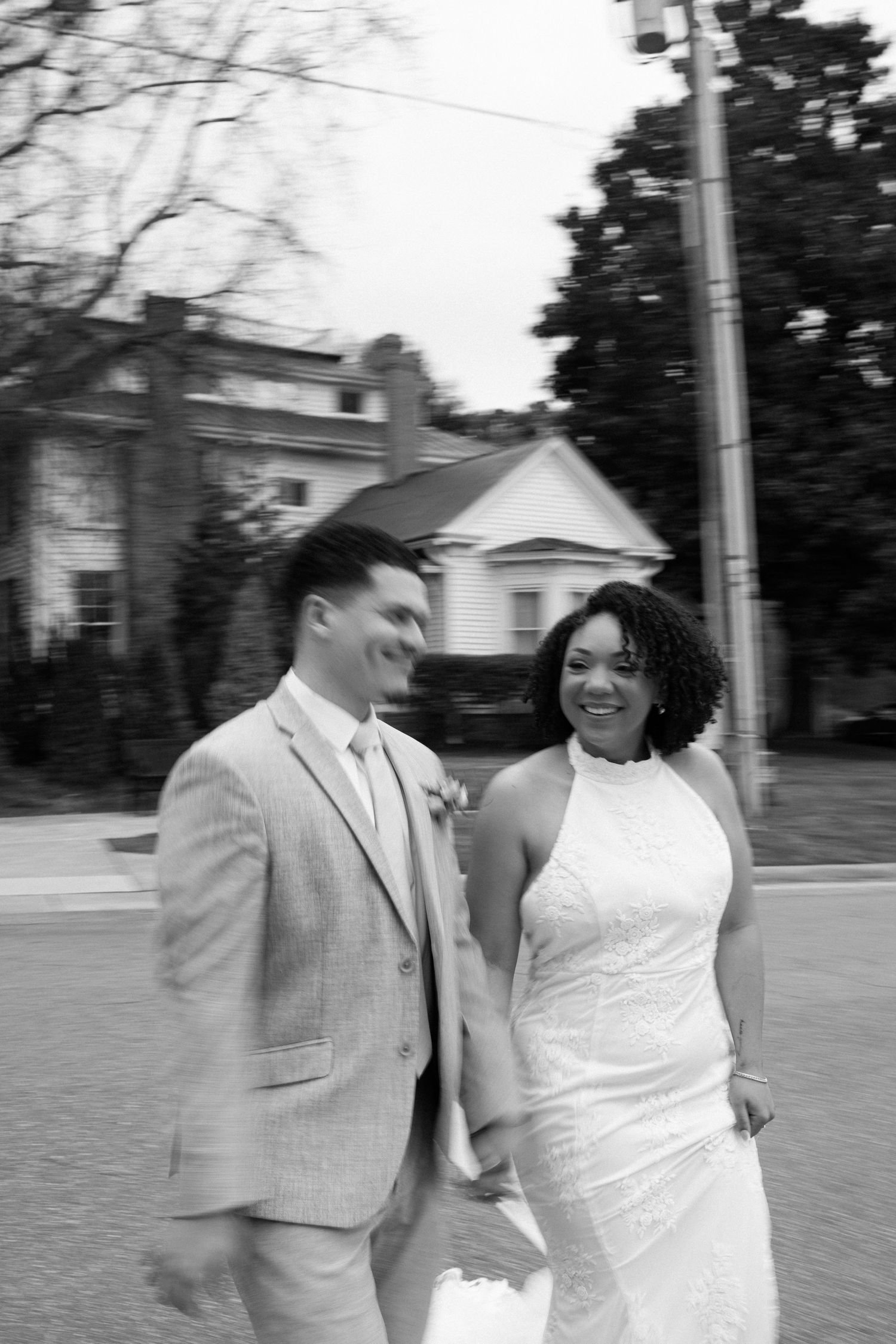 Black and white photo of a smiling bride and groom walking hand in hand outdoors on their wedding day.