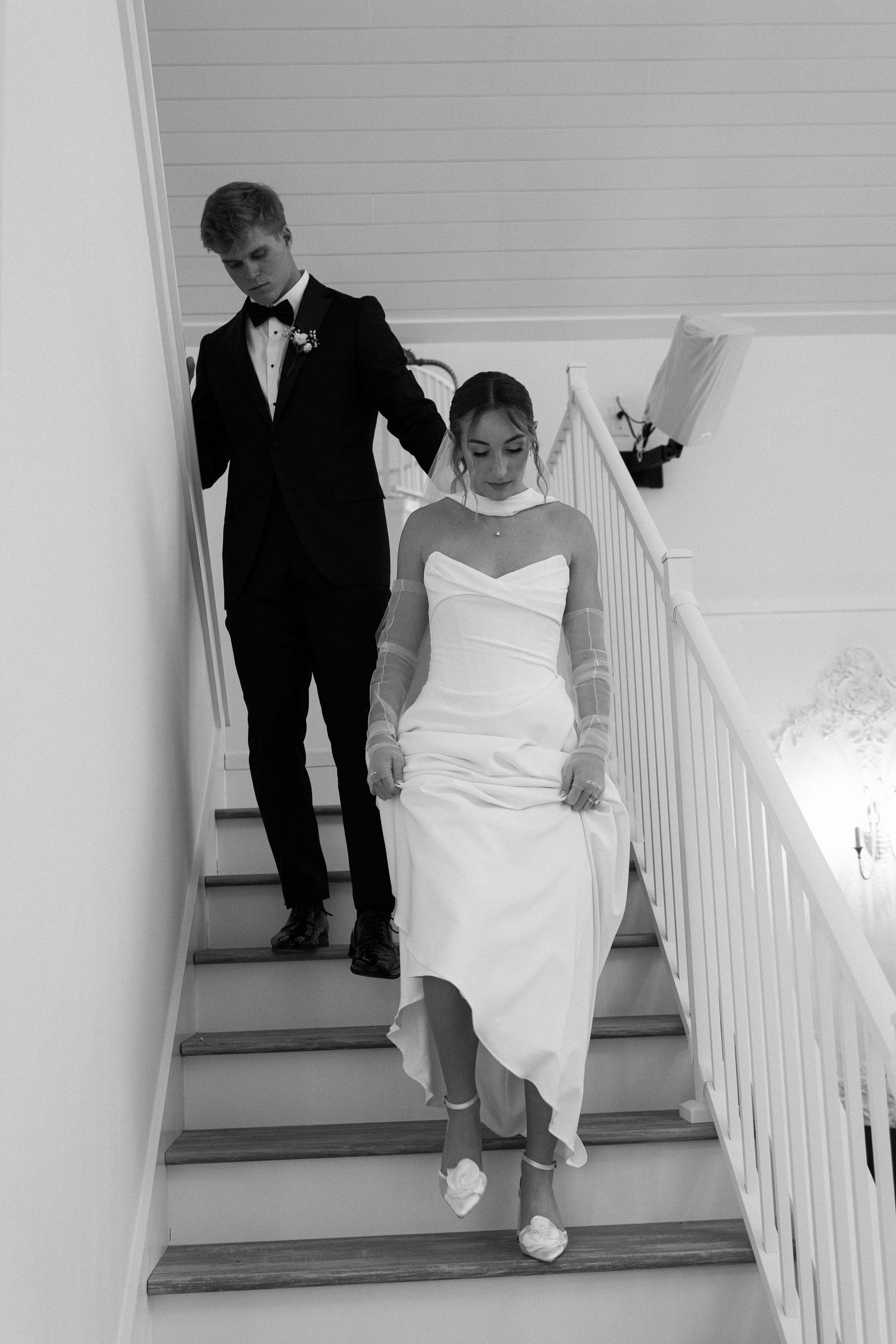 Black and white photo of bride and groom descending staircase on wedding day.