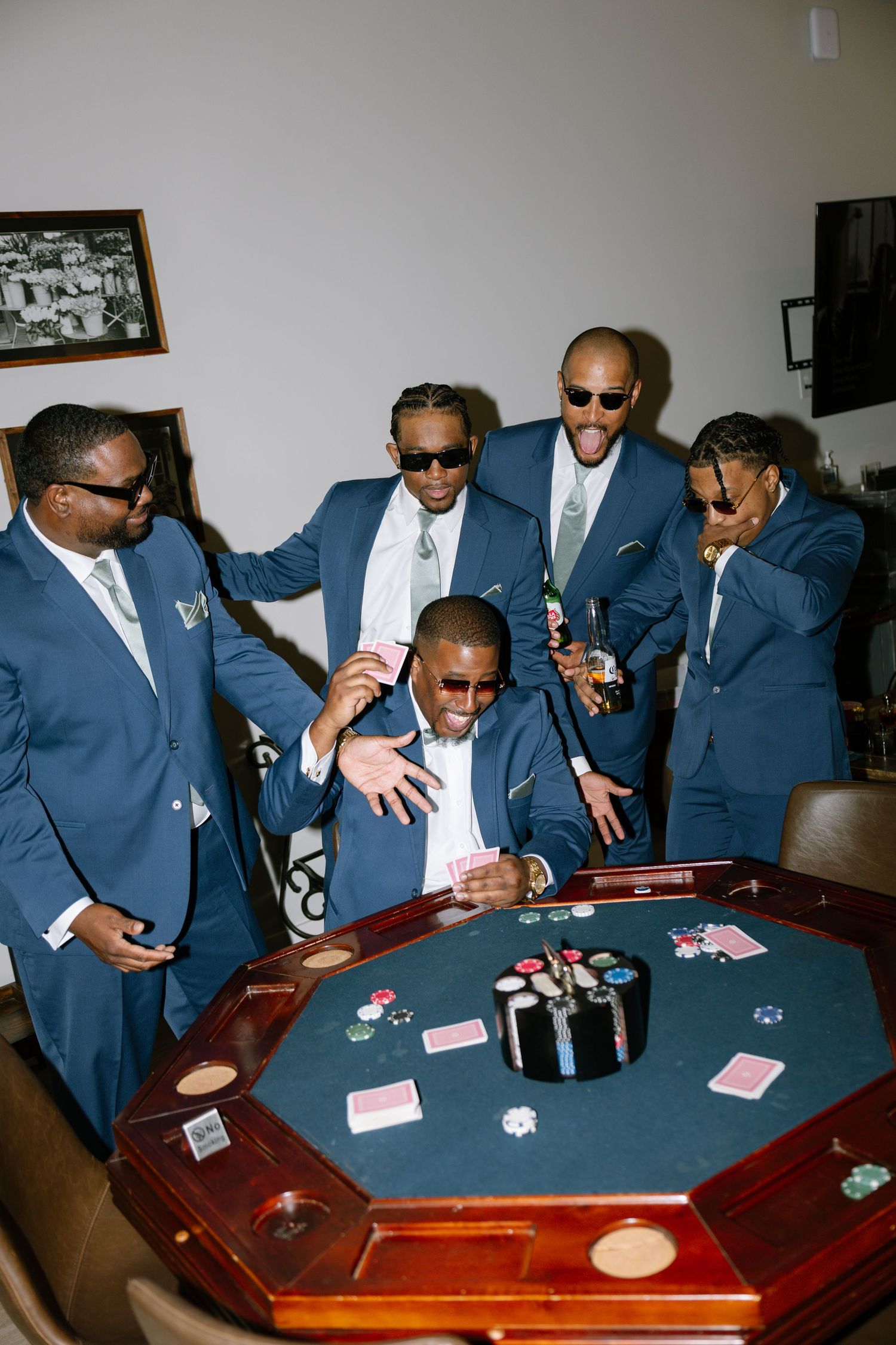 Group of men in blue suits gathered around a poker table with chips and cards during a celebration.