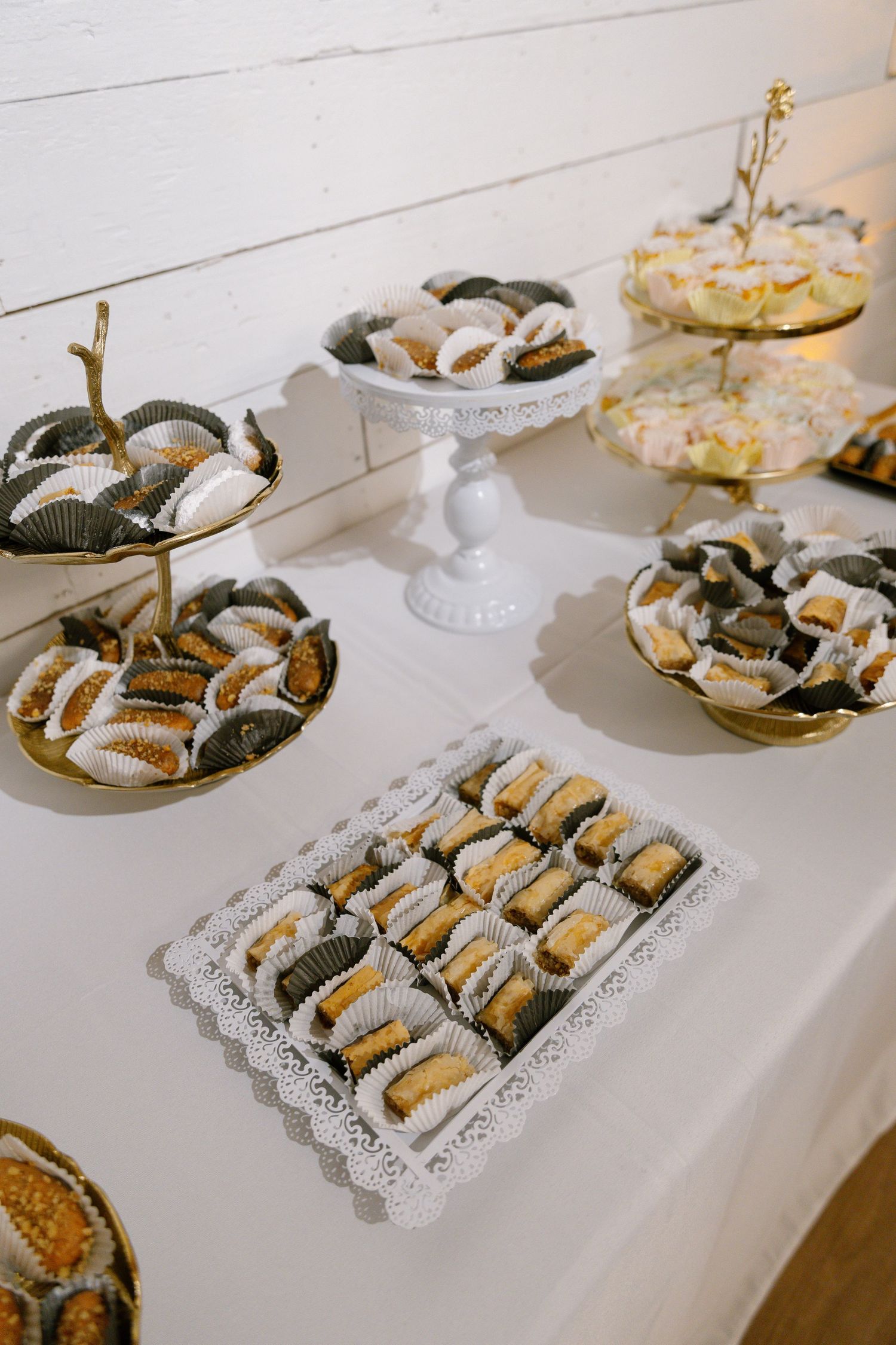 Elegant dessert table with assorted chocolates and pastries arranged on gold and white tiered stands.