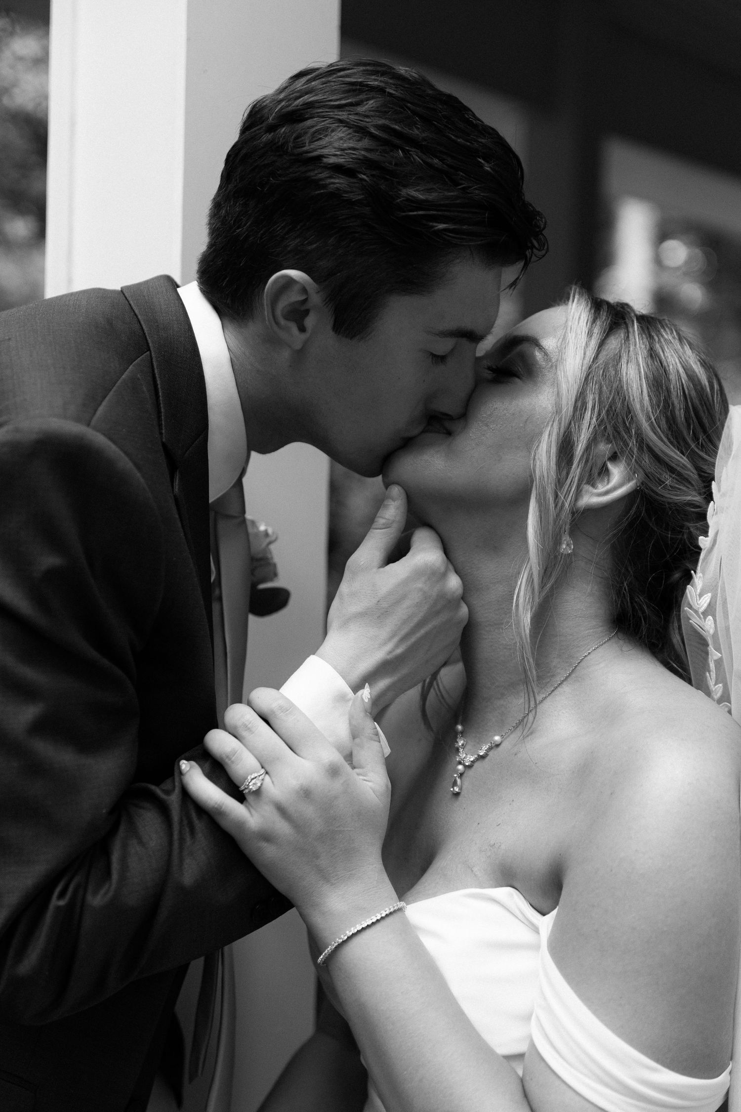 Black and white photo of a bride and groom sharing a romantic first kiss at their wedding ceremony.