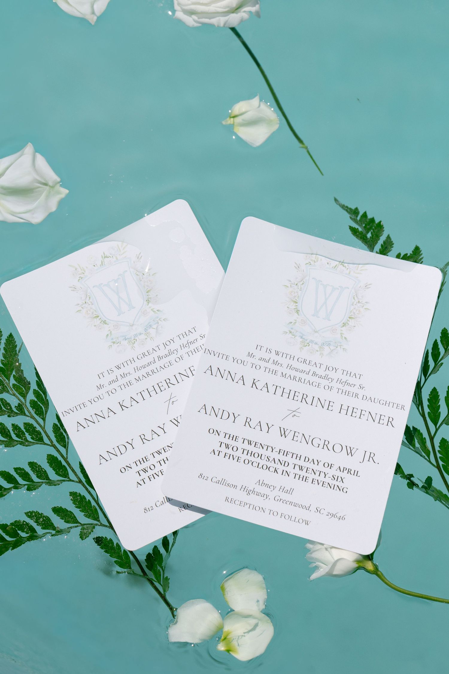 Elegant wedding invitations for Anna Katherine Hefner and Andy Ray Wengrow Jr. displayed on teal background with white flowers.