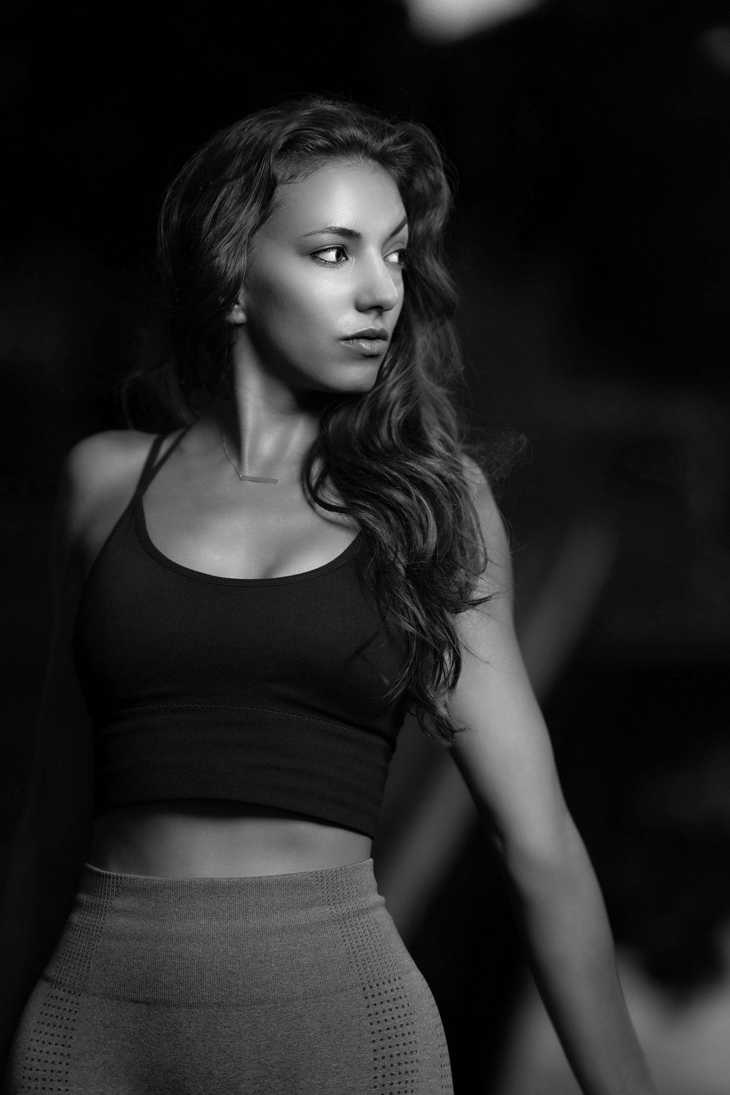 Black and white portrait of a fit young woman in a crop top and leggings, posing confidently in a gym setting.