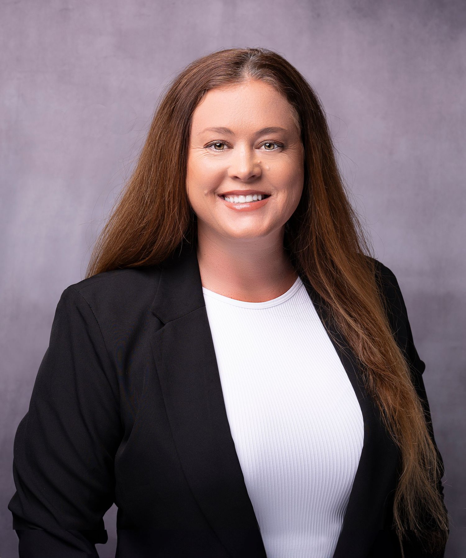 Professional headshot of a smiling woman with long auburn hair wearing a black blazer and white top.
