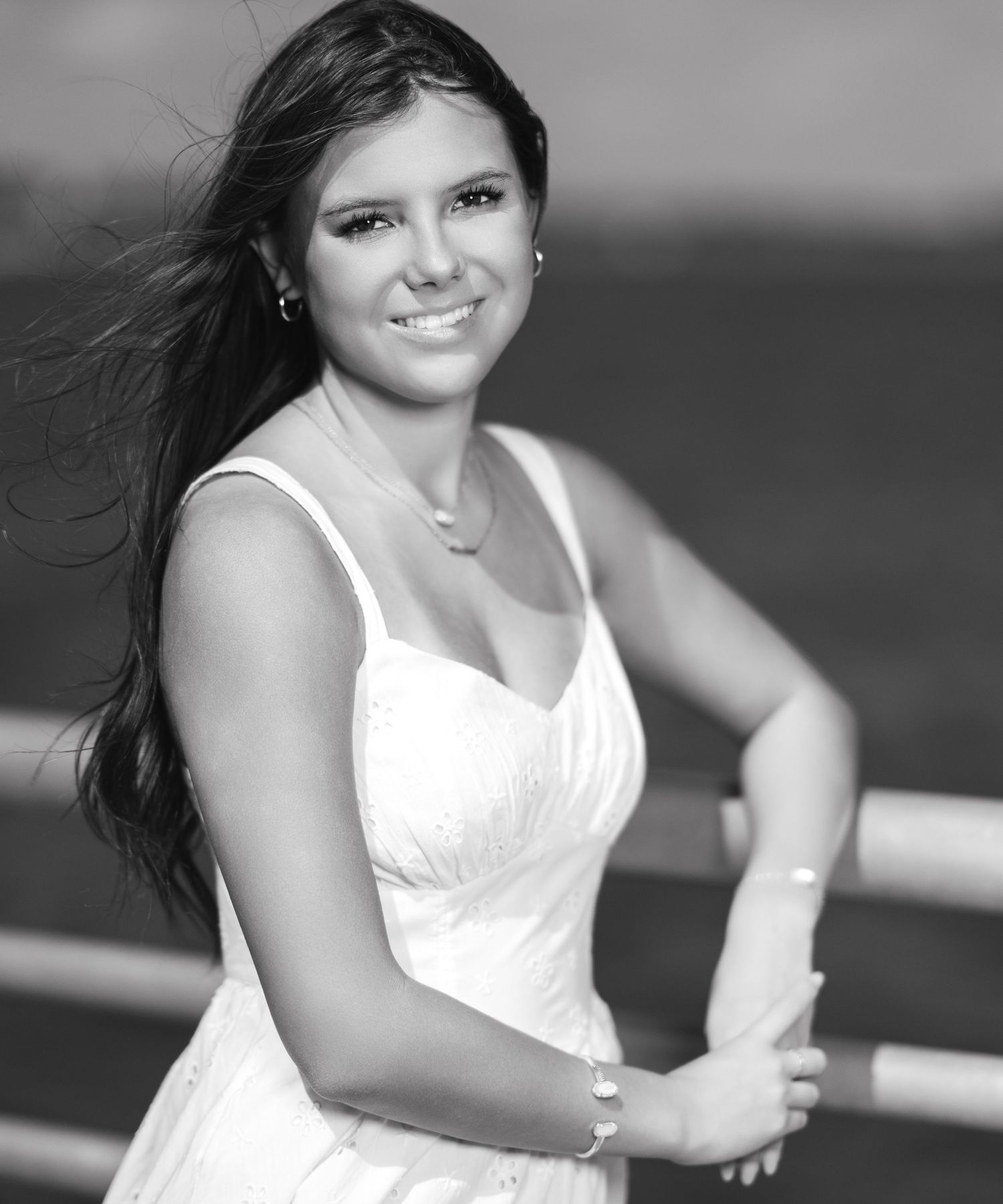 Black and white portrait of a smiling young woman in a white dress with long dark hair outdoors.
