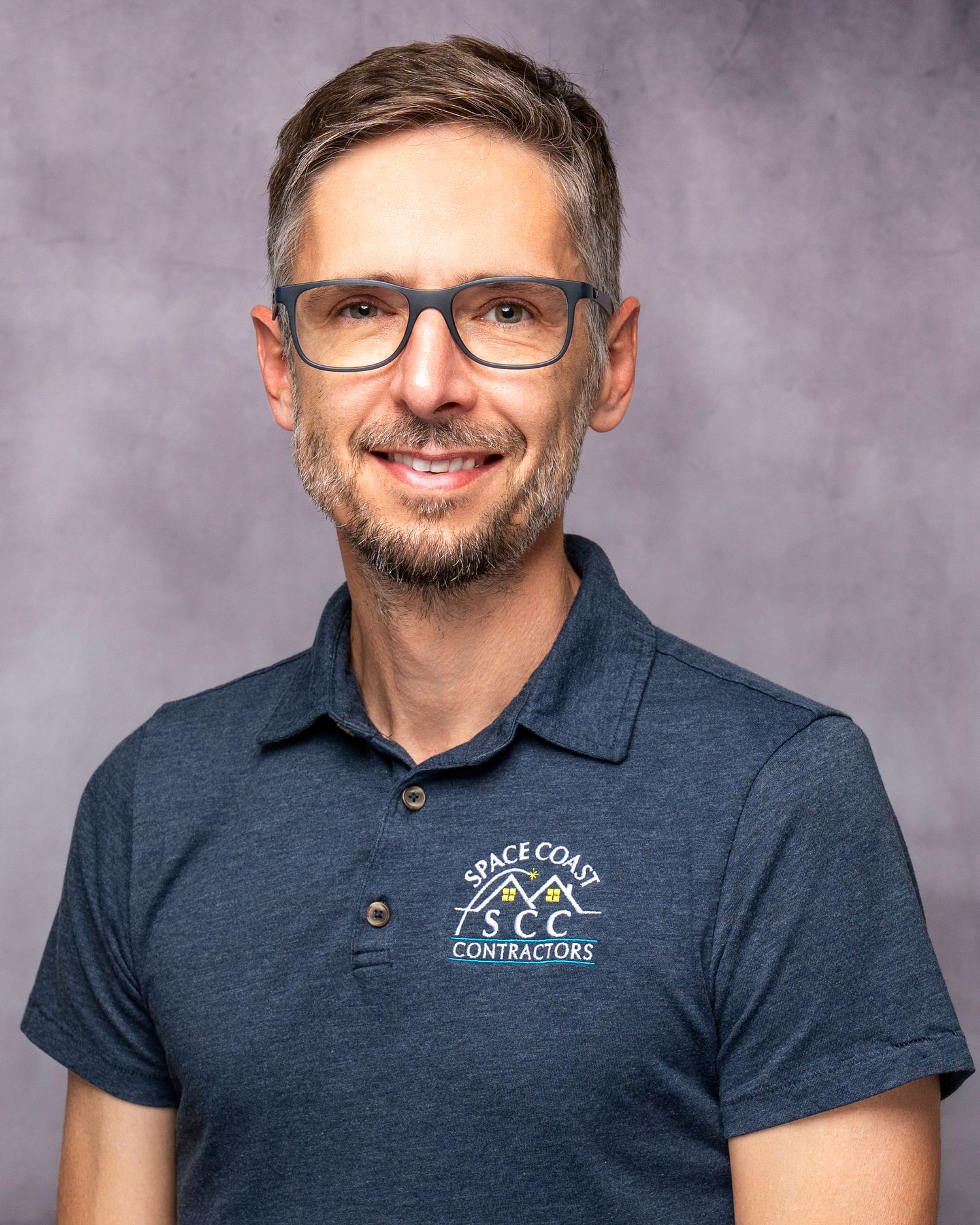 Man in Space Coast Contractors polo shirt and glasses smiling in professional headshot photo.