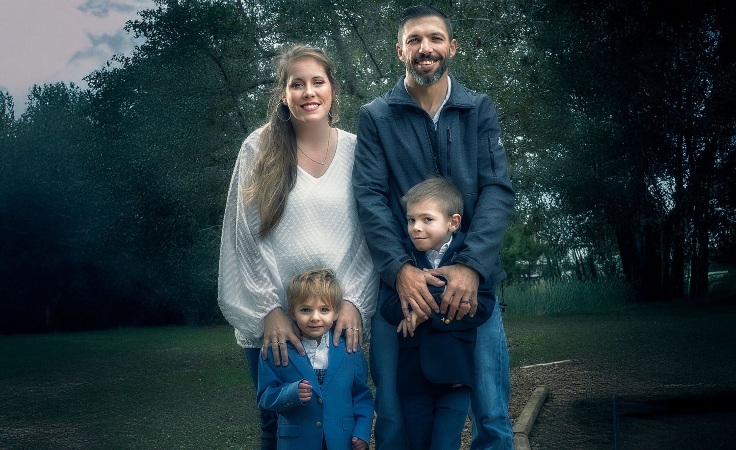 Family of four posing outdoors in a misty park, parents with two young children smiling for a portrait.