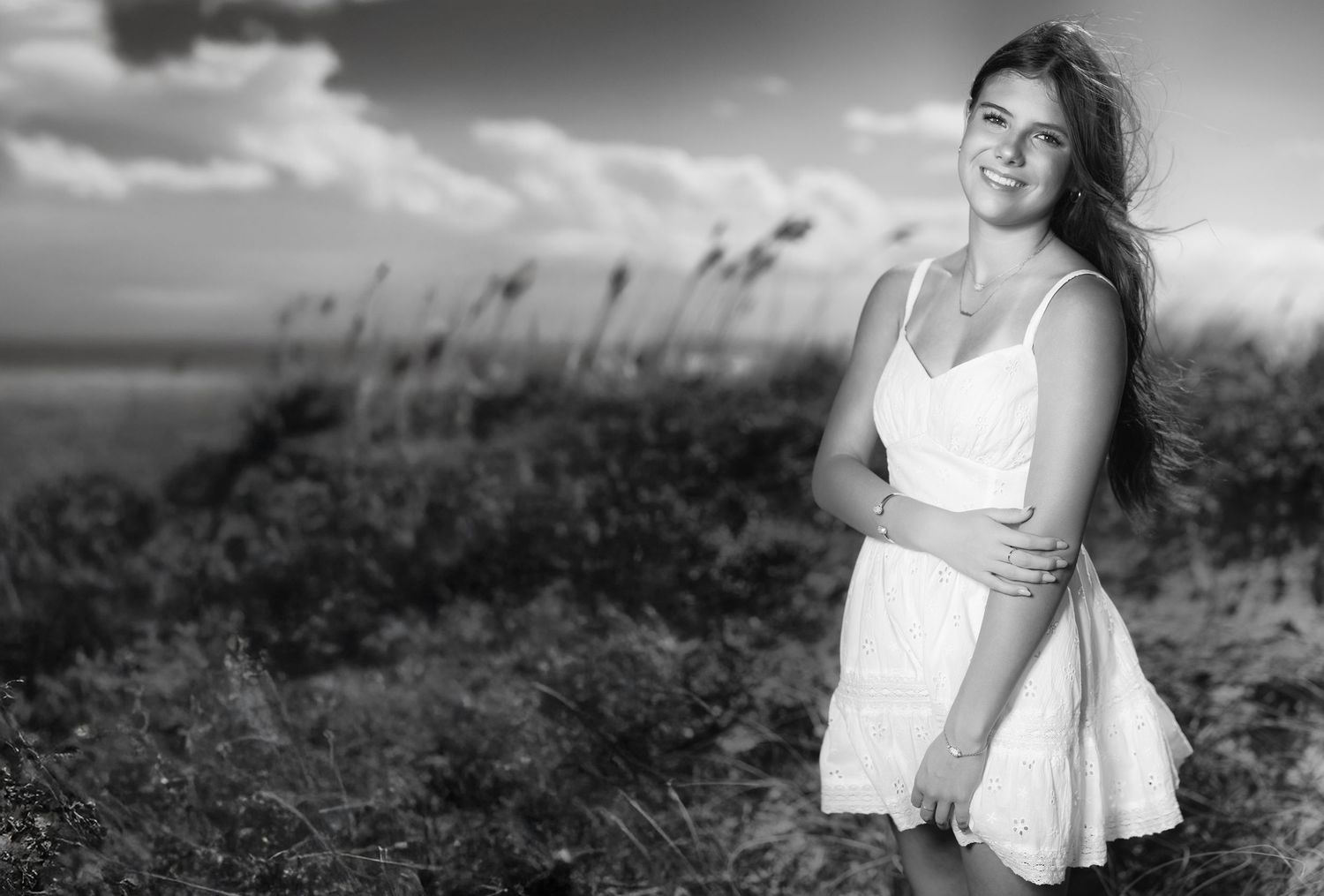 Young woman in white dress smiling on a breezy beach, black and white portrait photography.