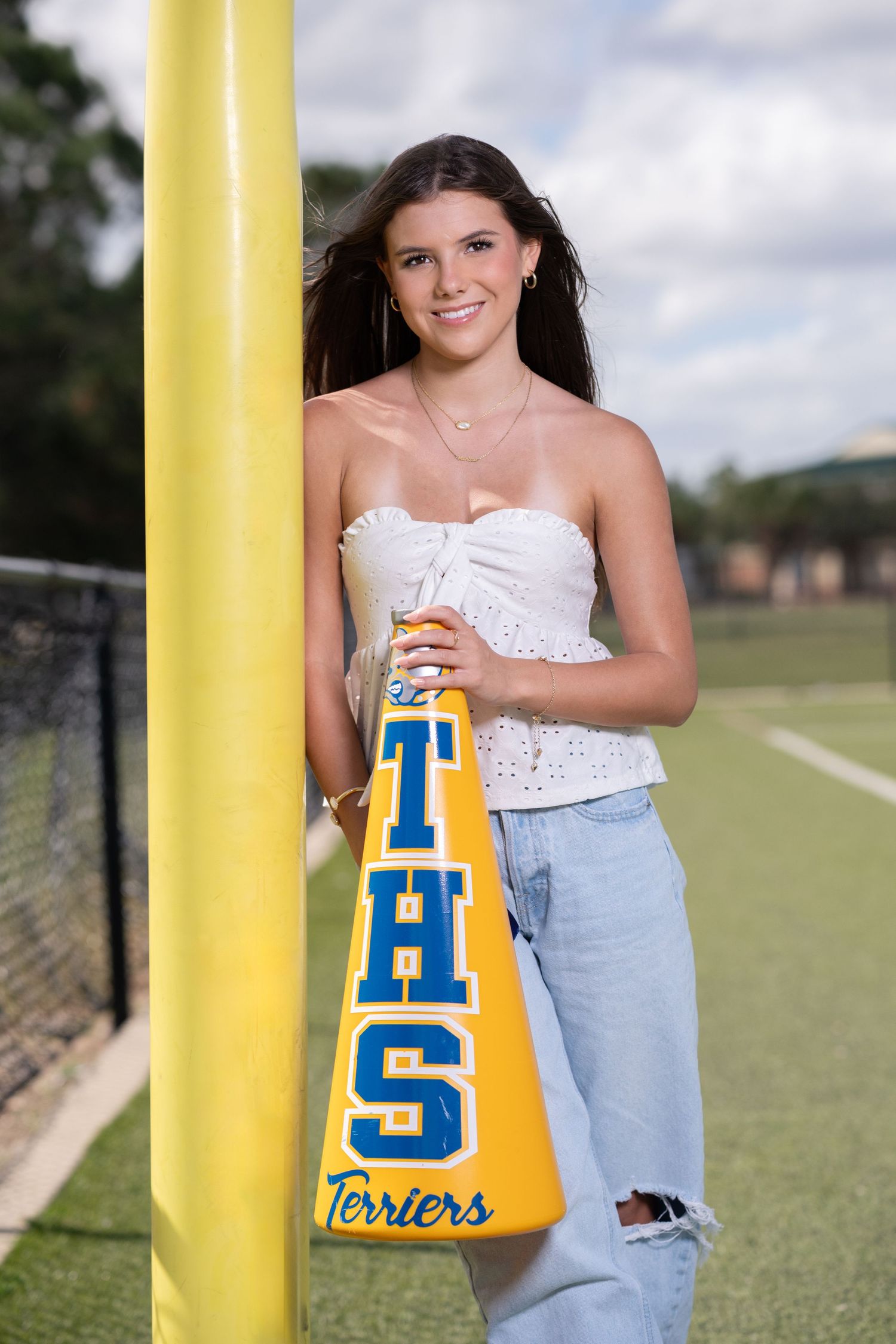 Teen girl leaning on yellow goal post holding THS Terriers megaphone on a green football field.