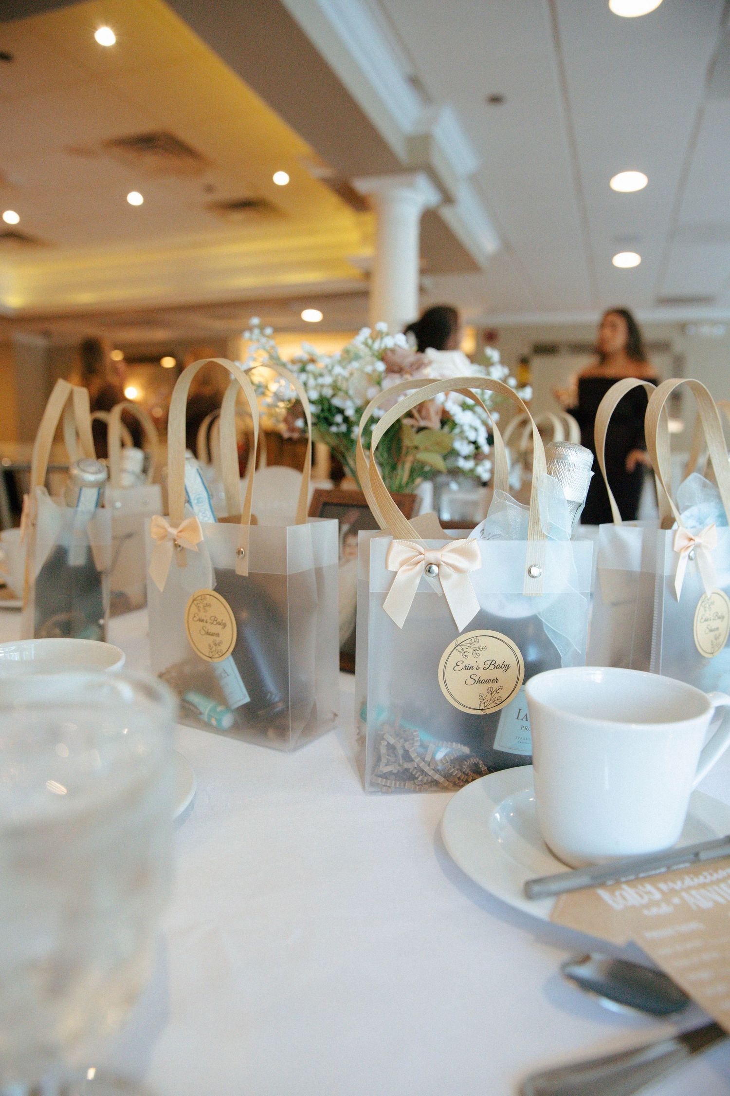 Elegant frosted gift bags with ribbon bows and tags arranged on white tablecloth at bridal shower.