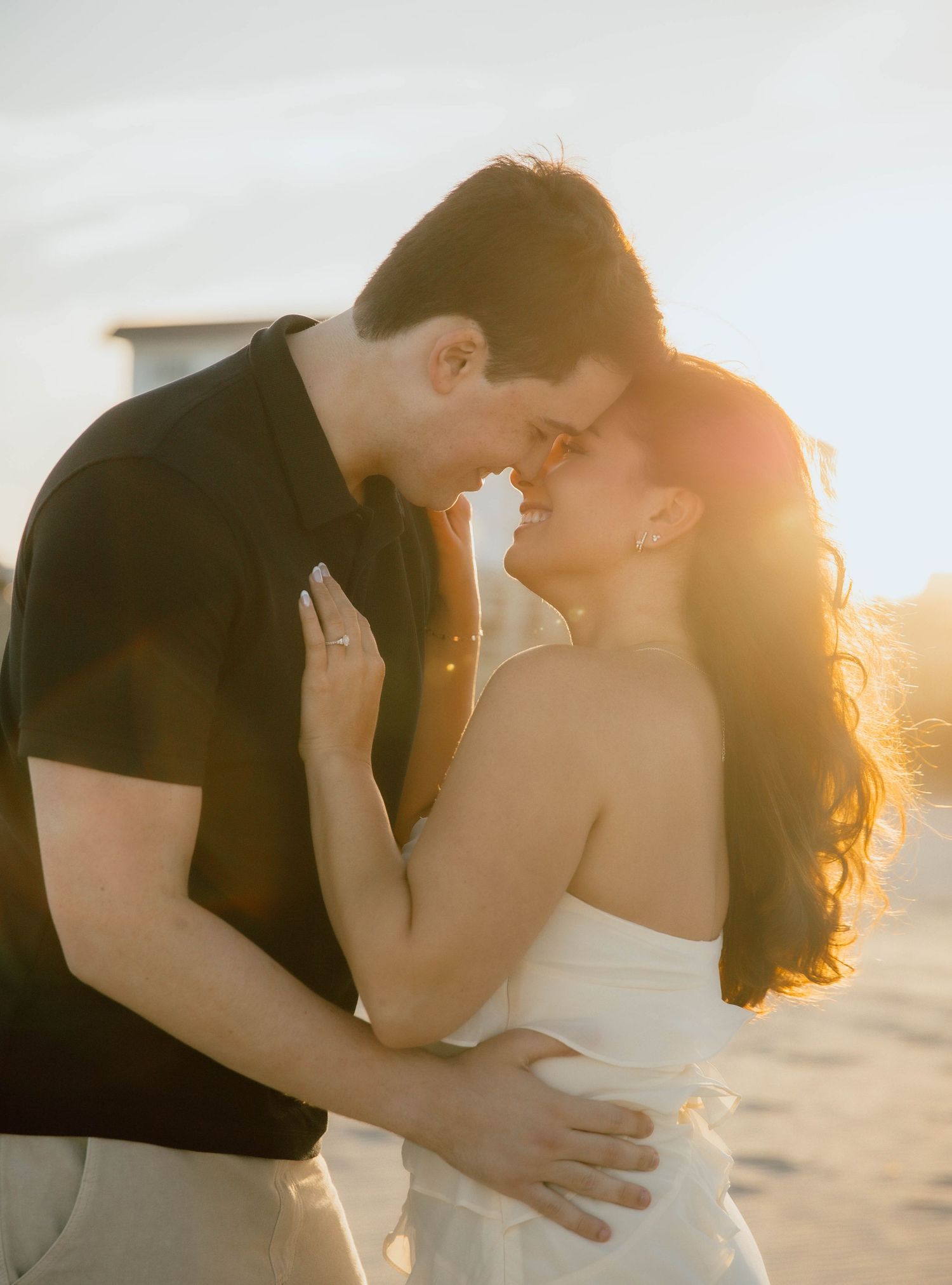 Romantic couple embracing at golden hour sunset on a beach, foreheads touching tenderly.